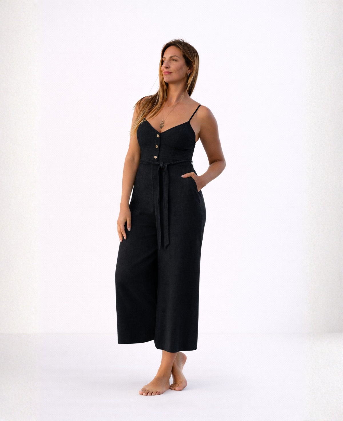 Angled front studio view of the Bella Byron Linen Jumpsuit in black, highlighting the fitted bodice, button detail, adjustable straps, waist tie belt and relaxed cropped palazzo silhouette.