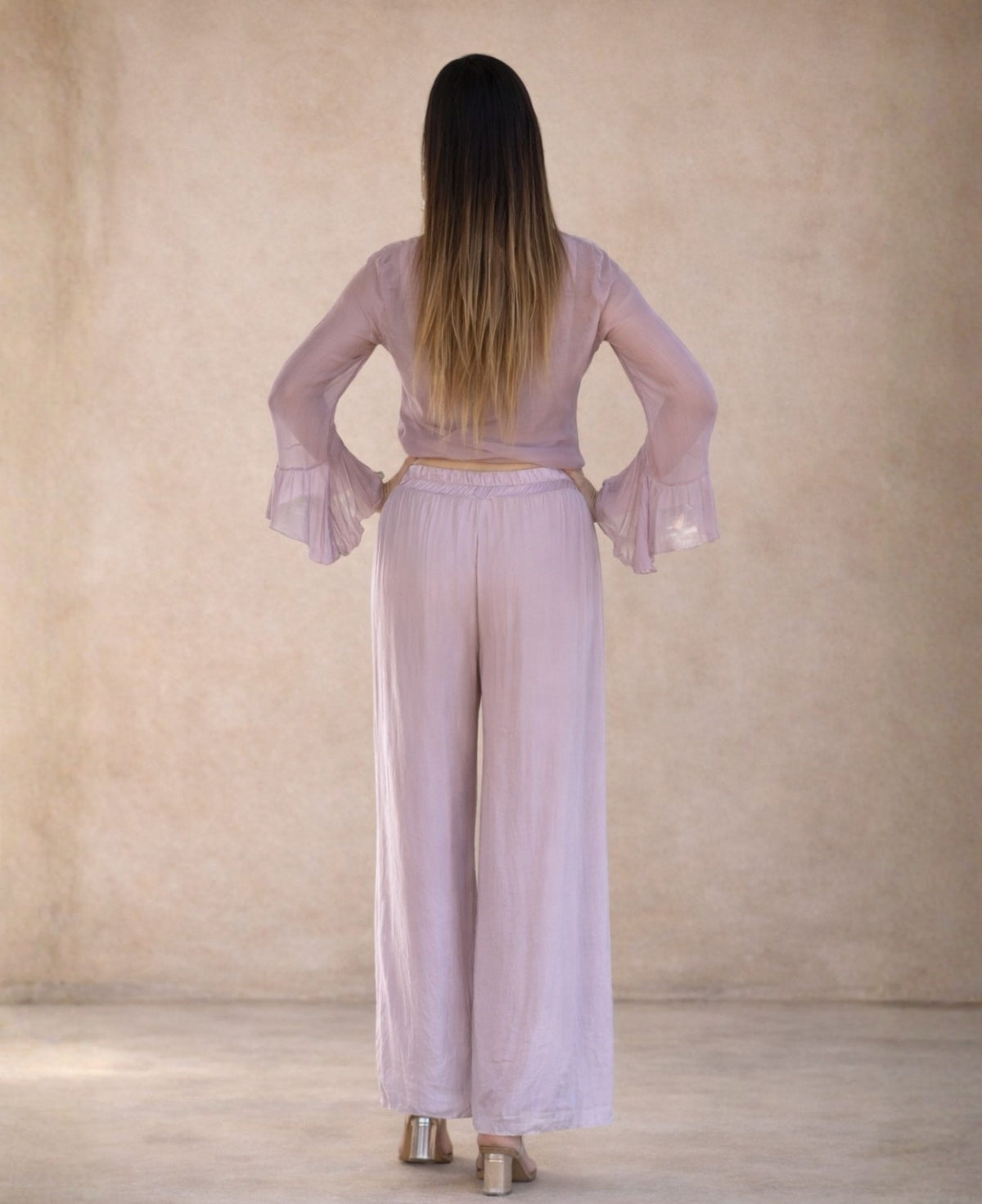 Back view of rose silk blend pants showing relaxed wide leg silhouette and elasticated waistband, styled in a soft neutral studio setting.