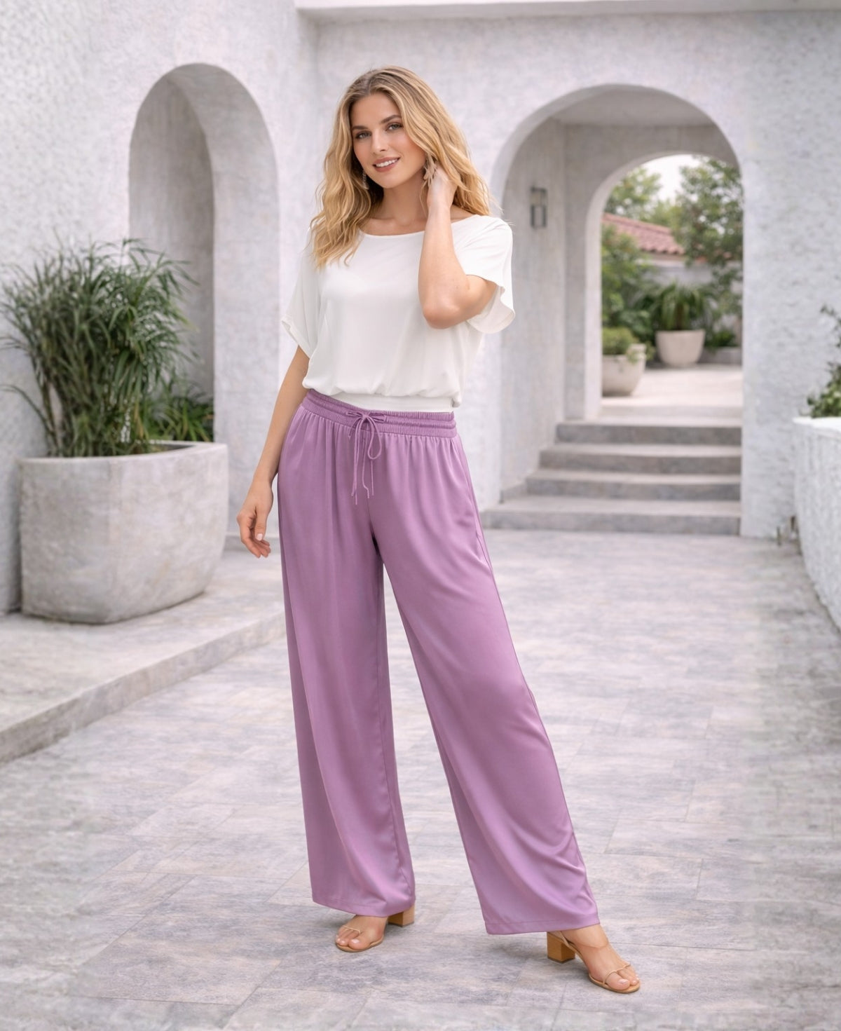 Plum Juliette satin pants styled with a light top, showing elegant satin sheen and soft drape on a Mediterranean terrace