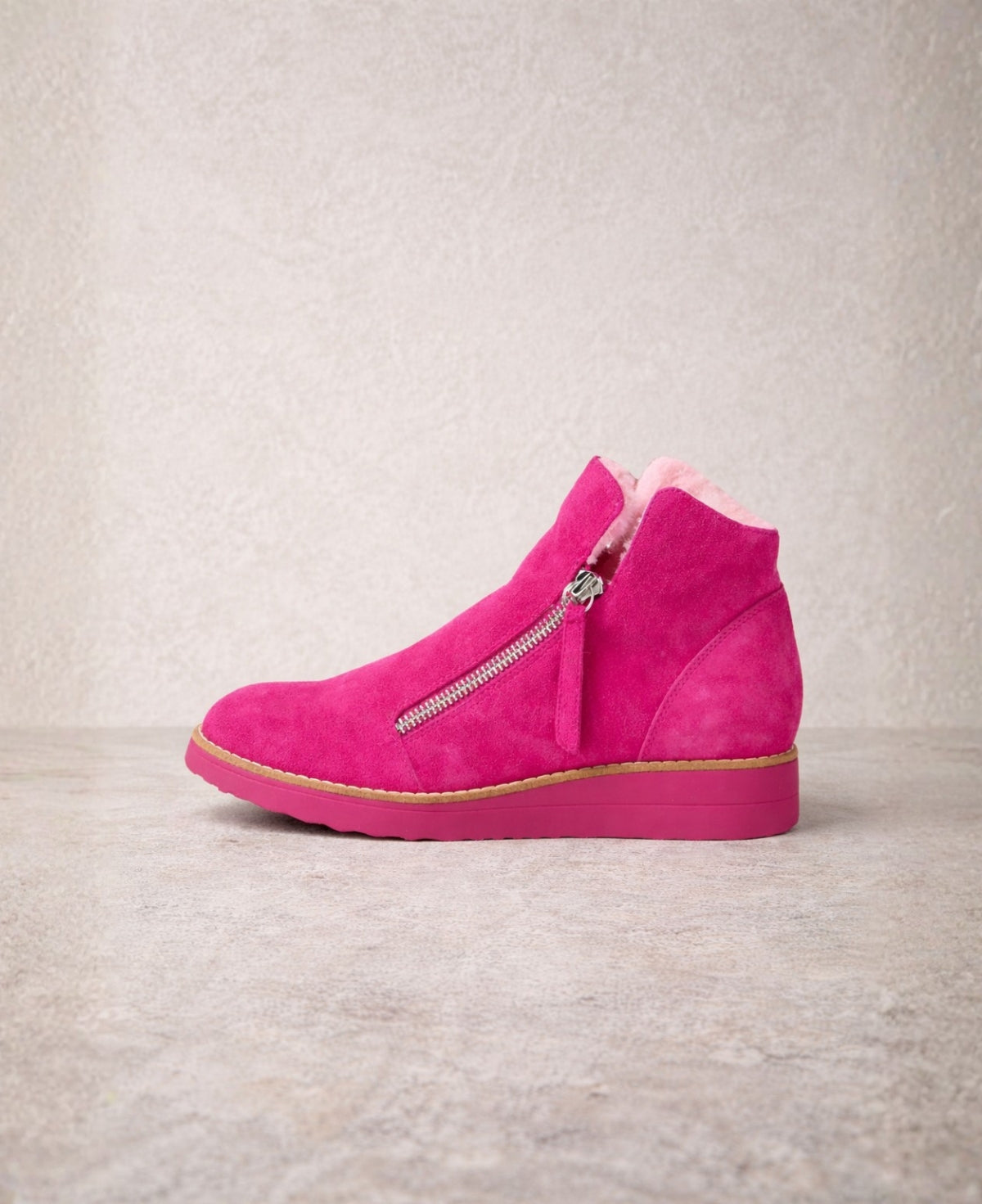 Side profile of Opal fuchsia suede ankle boots with twin zip fastening, faux fur lining and low wedge sole on a neutral stone background.