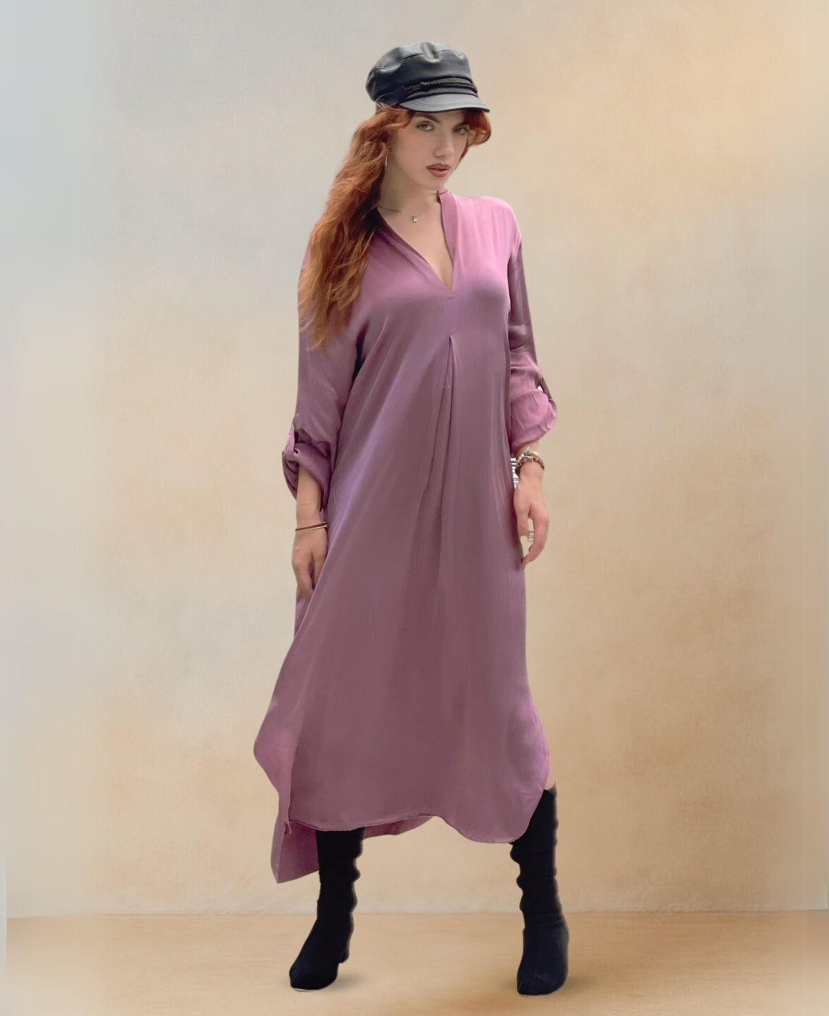 Front view of the Valene Maxi Dress in dusty pink, crafted from luxurious satin with a soft sheen. Features a graceful V-neckline, flowing silhouette, and side splits for elegant movement. Worn with boots.
