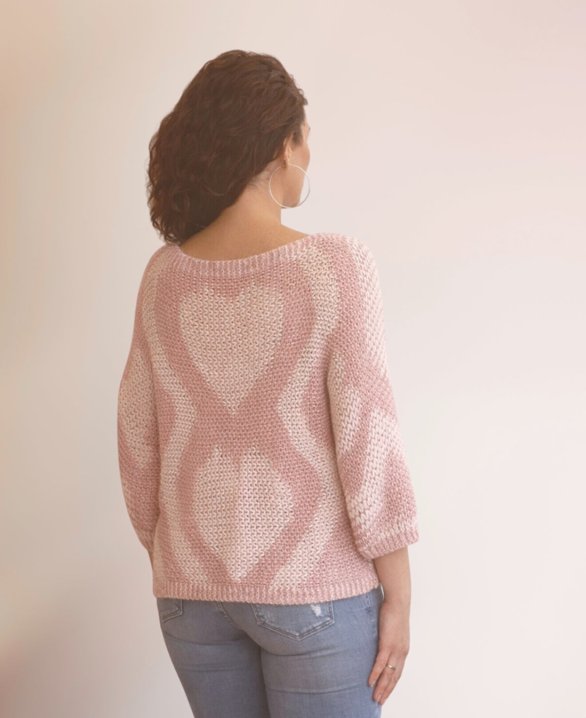 Back view of the Valentine Wool Blend Jumper in Blush showing the heart knit pattern across the back, styled with blue jeans in a neutral studio setting.
