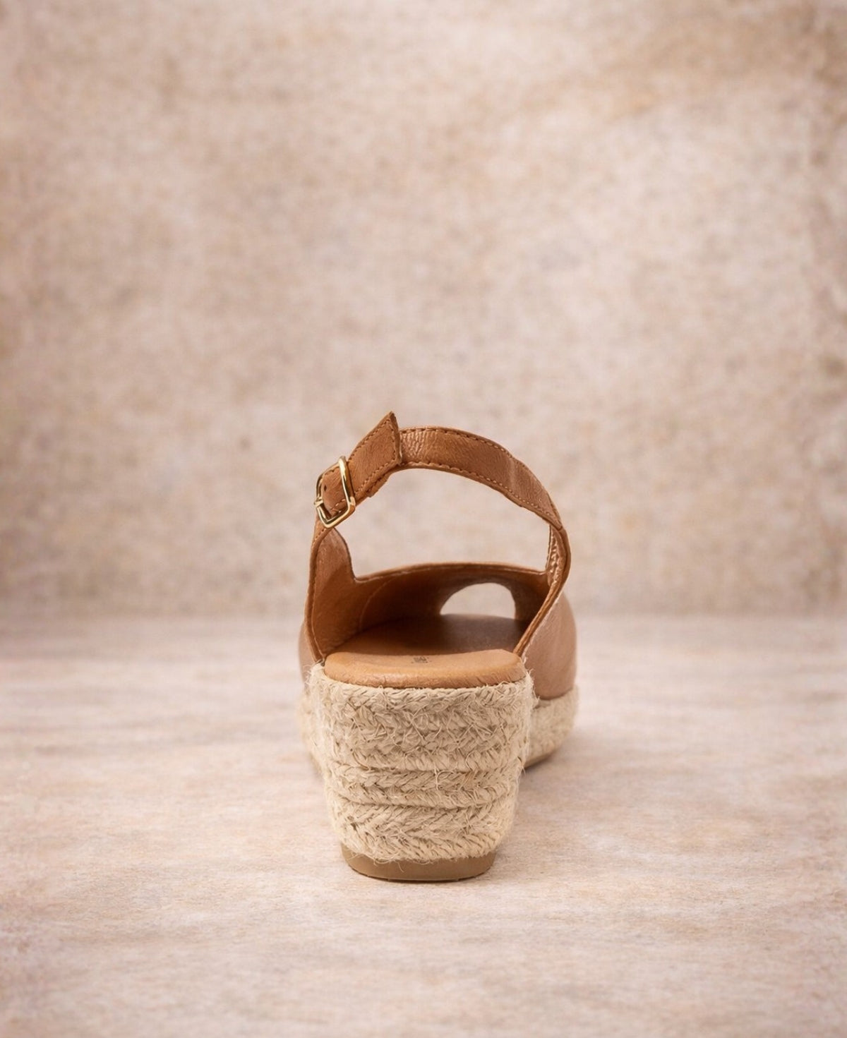 Tan leather espadrille wedge sandal with slingback strap and jute heel, shown from the back on a soft stone background