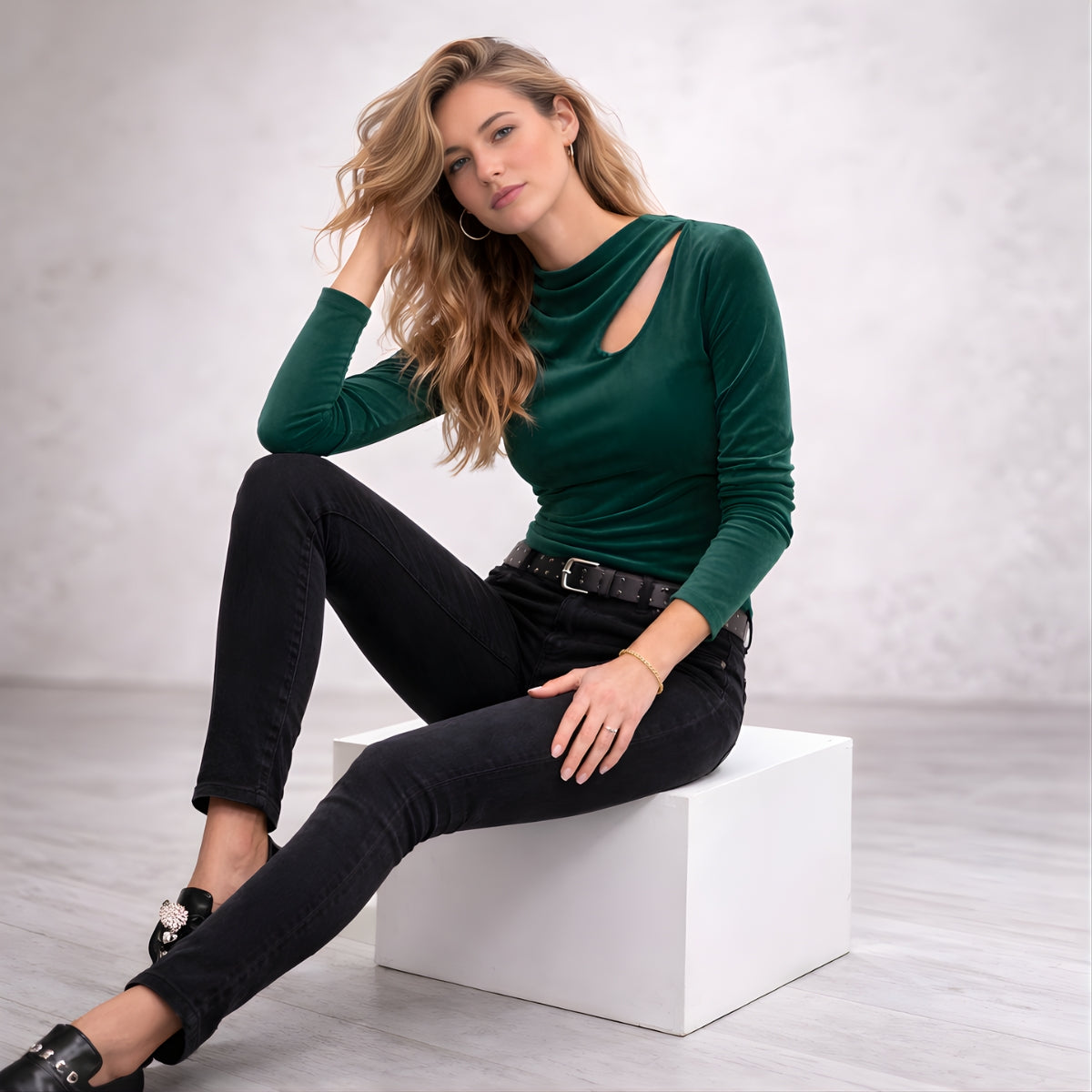 Stylish woman wearing an elegant green long sleeve top with black jeans in a minimalist studio setting