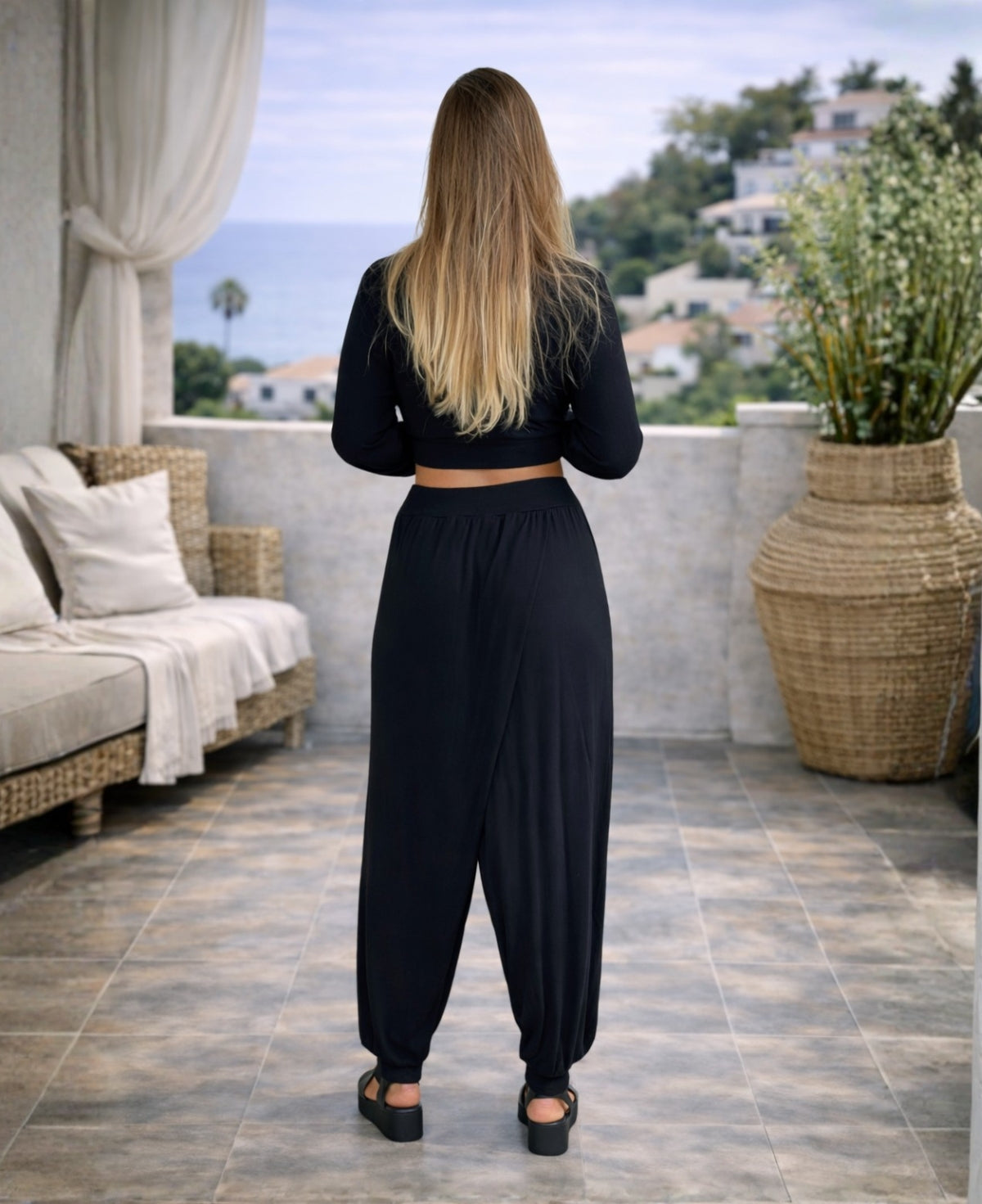 black aladina knit harem pants back view styled on a woman overlooking a coastal mediterranean setting with relaxed silhouette
