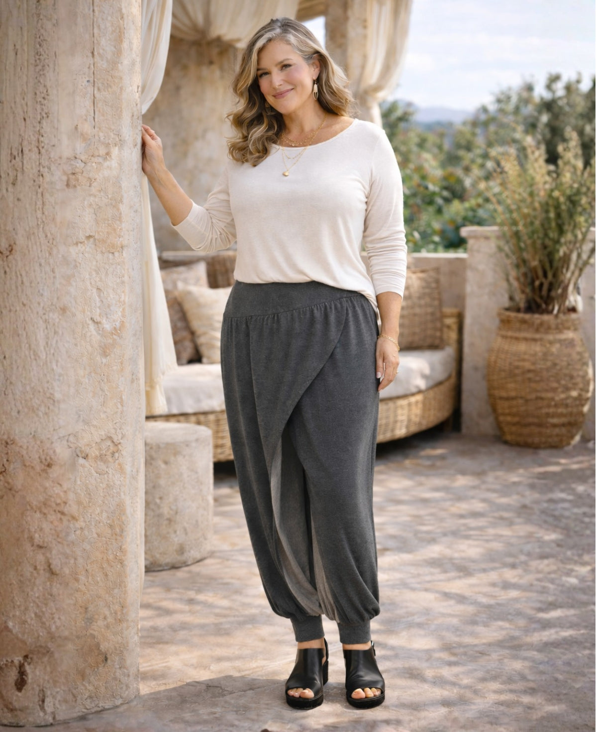 charcoal aladina knit harem pants styled on a mature woman in a mediterranean outdoor space highlighting soft drape and layered front