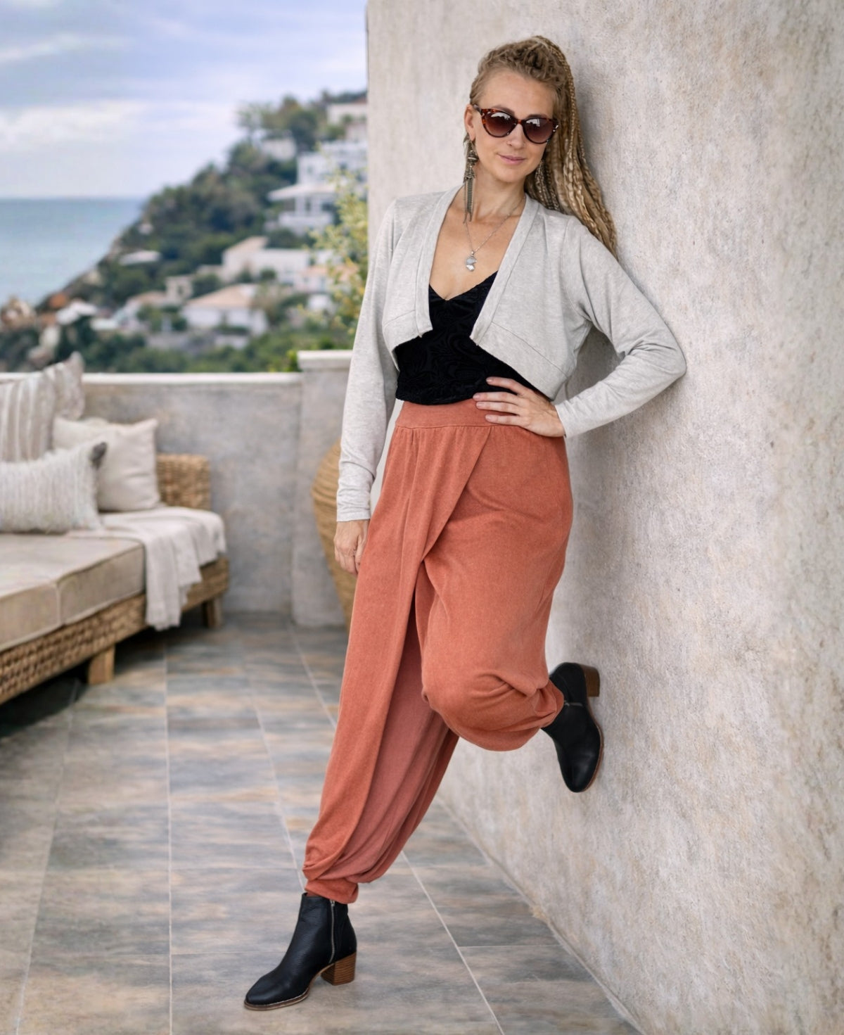 copper aladina knit harem pants styled on a woman leaning against a wall in a mediterranean outdoor setting with layered crossover front