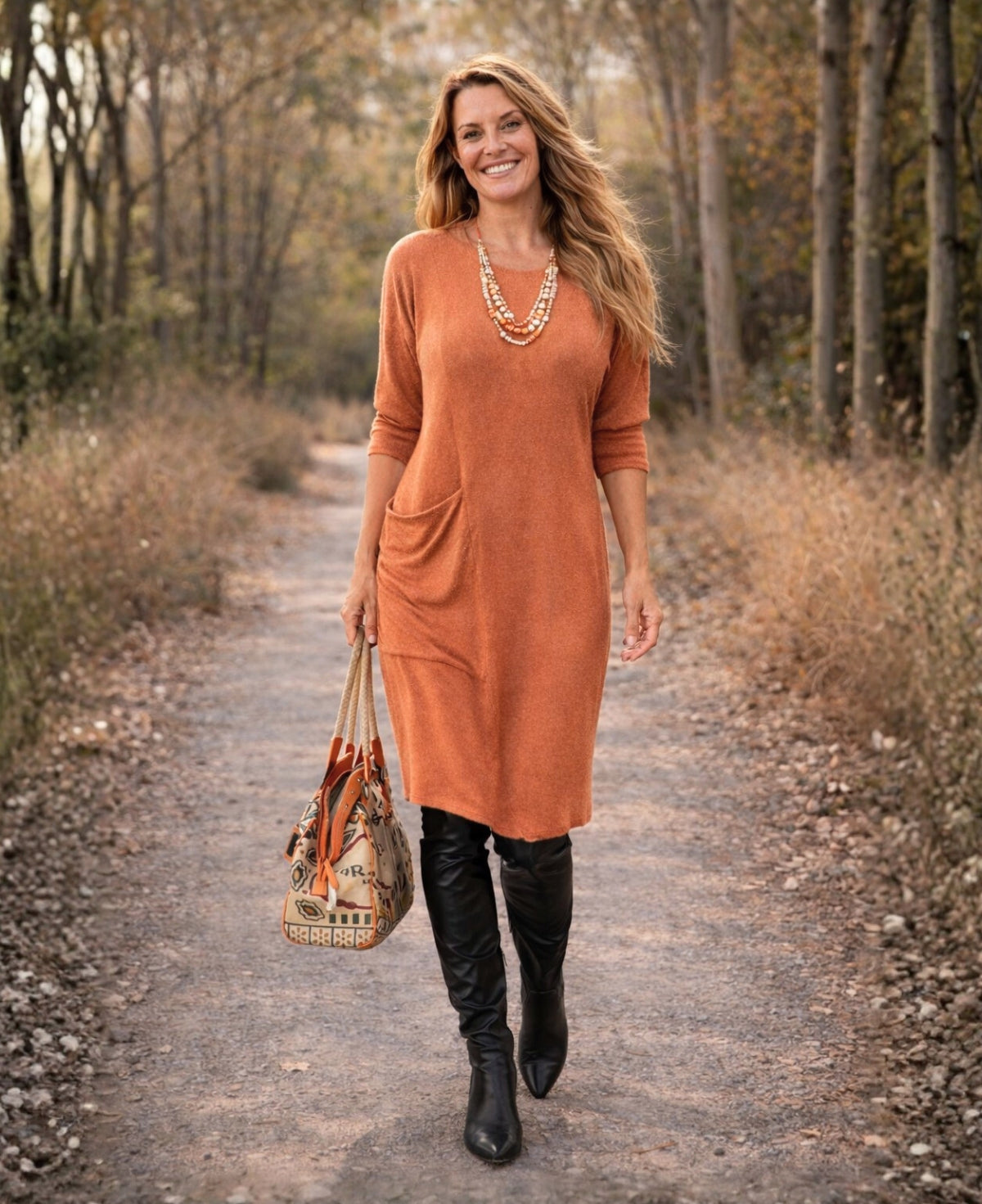 Blonde model wearing the Alessandra rust knit dress with smooth hemline and side pocket, styled for winter layering