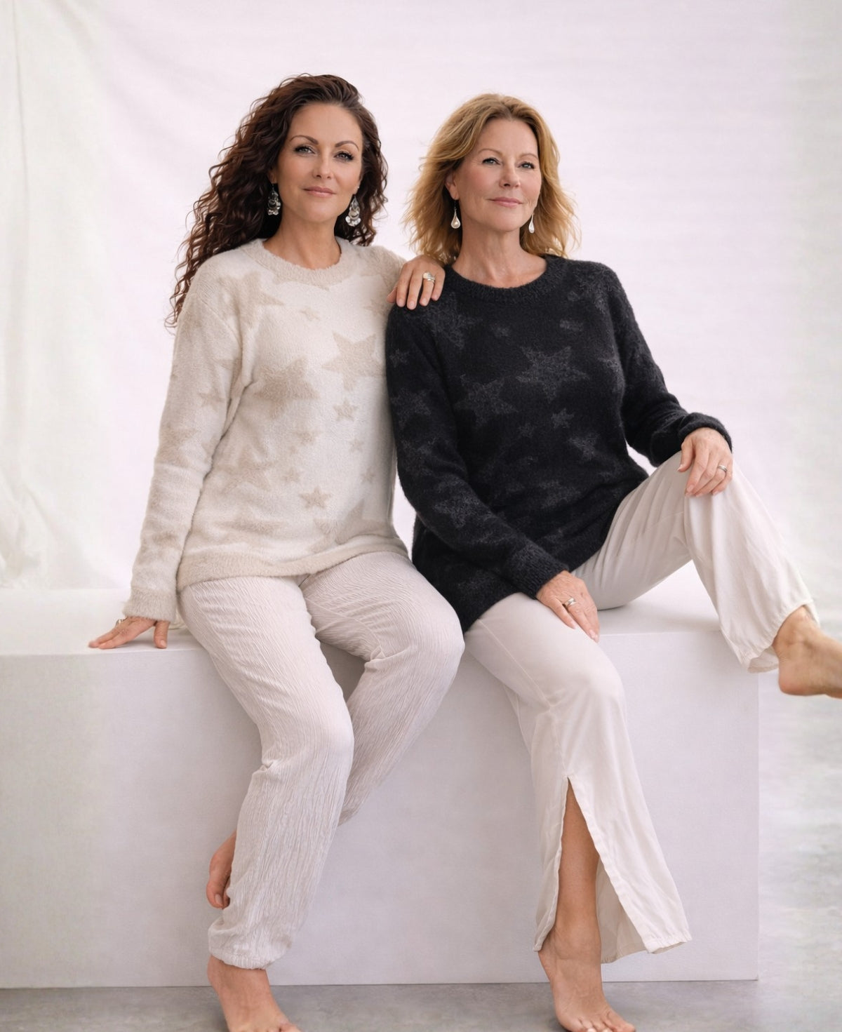 Two women wearing beige and black Apollo star sweaters seated together in a minimalist studio setting