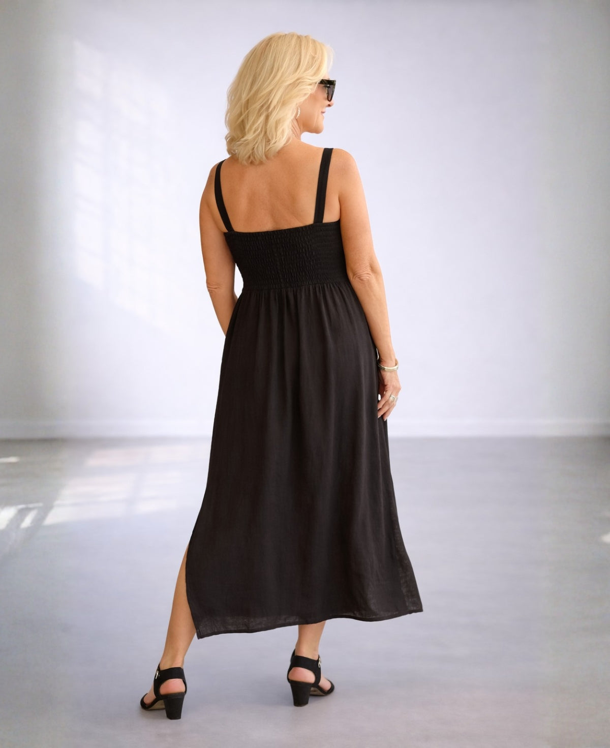Back angled view of the Ava black linen dress showing the shirred elastic back and flowing skirt.