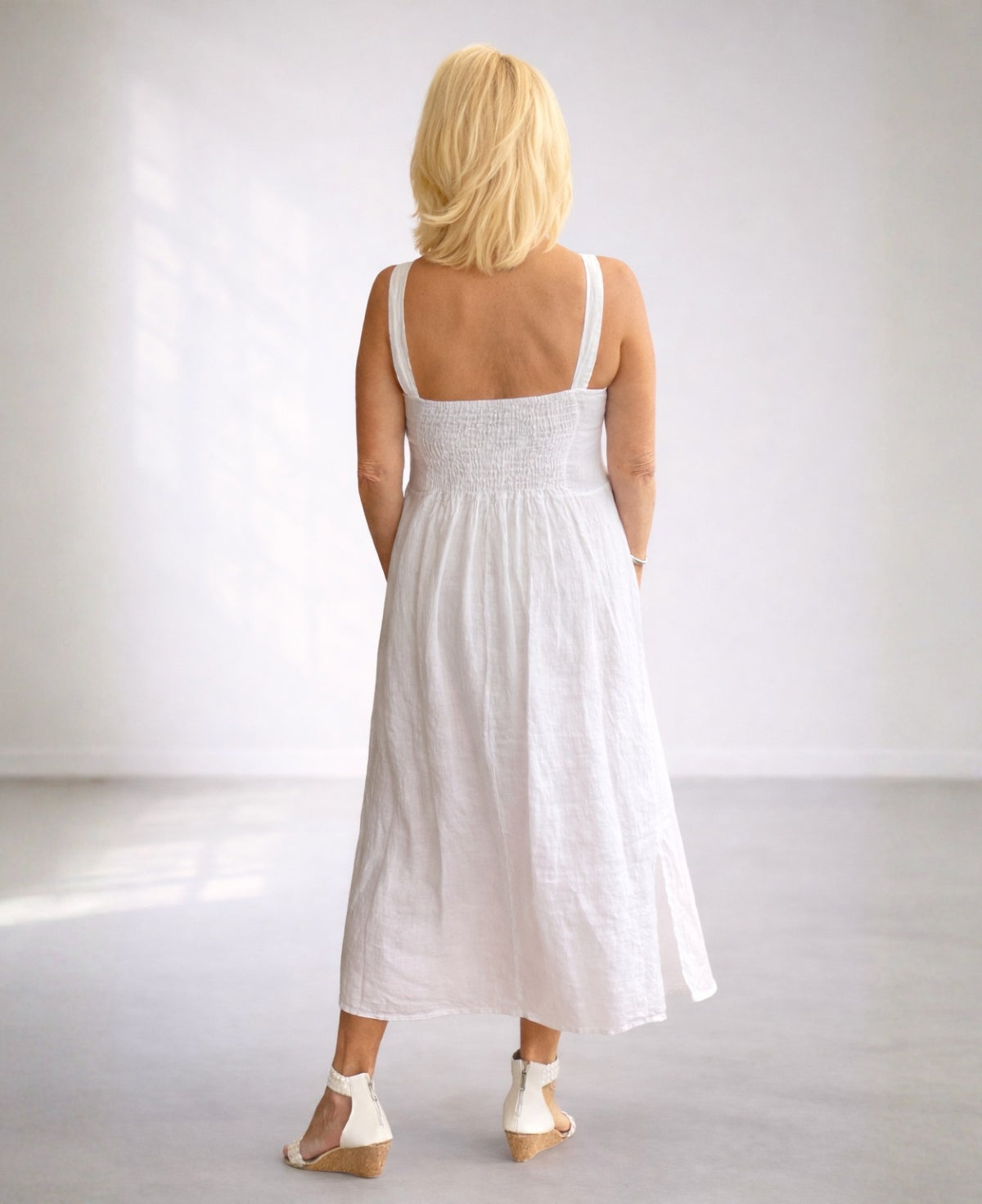 Back view of the Ava white linen dress showing shirred elastic back and shoulder straps in a soft studio setting.