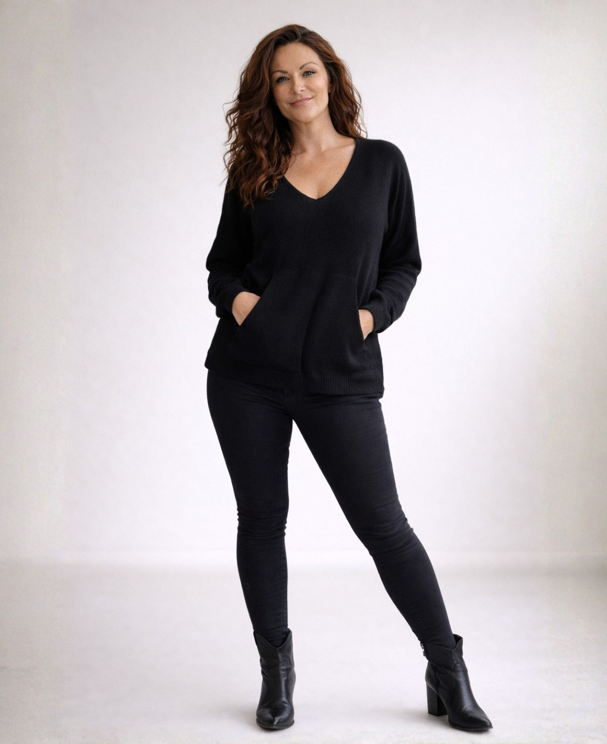Full body view of black cashmere V-neck sweater styled in minimalist studio setting