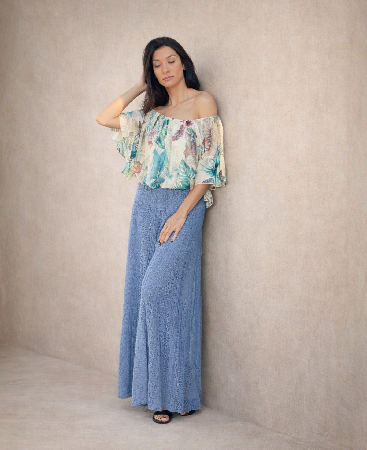 Woman wearing soft blue boho lace wide leg pants with an off-shoulder floral top, styled in a neutral studio setting highlighting the lace texture and flow.