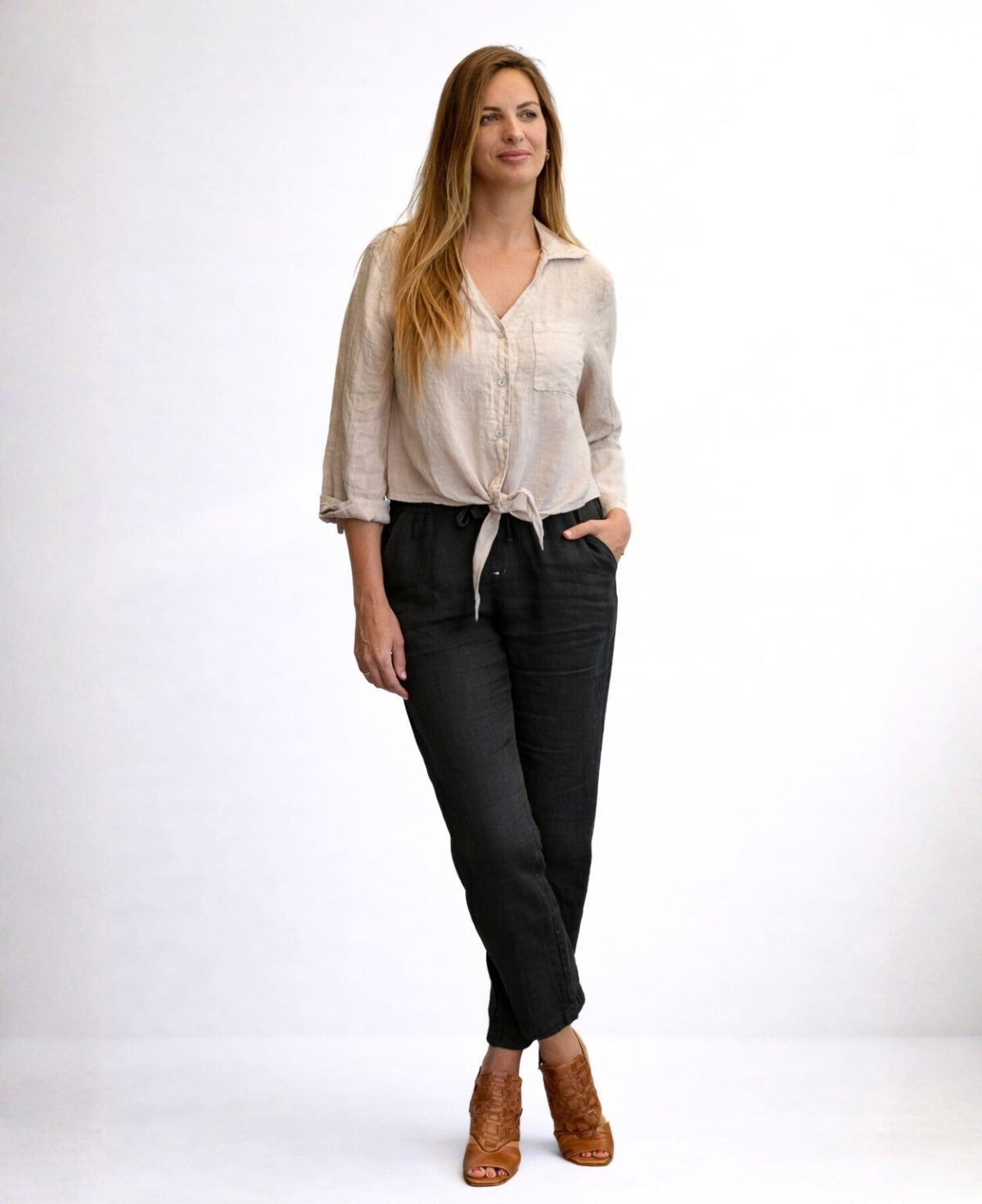Model wearing black Brooklyn linen pants in full body front view with crossed legs, relaxed fit linen pants with elastic waist, studio setting Australia