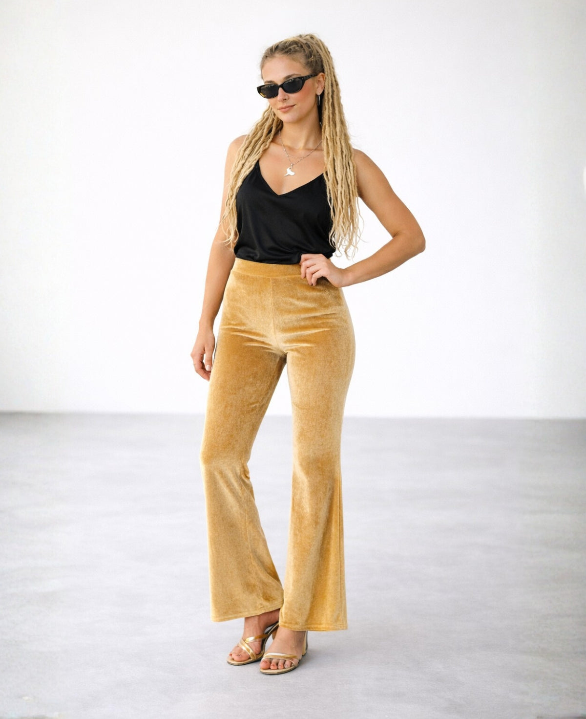 Model wearing camel velour flare pants with flat waistband and wide leg, styled with black top, studio background