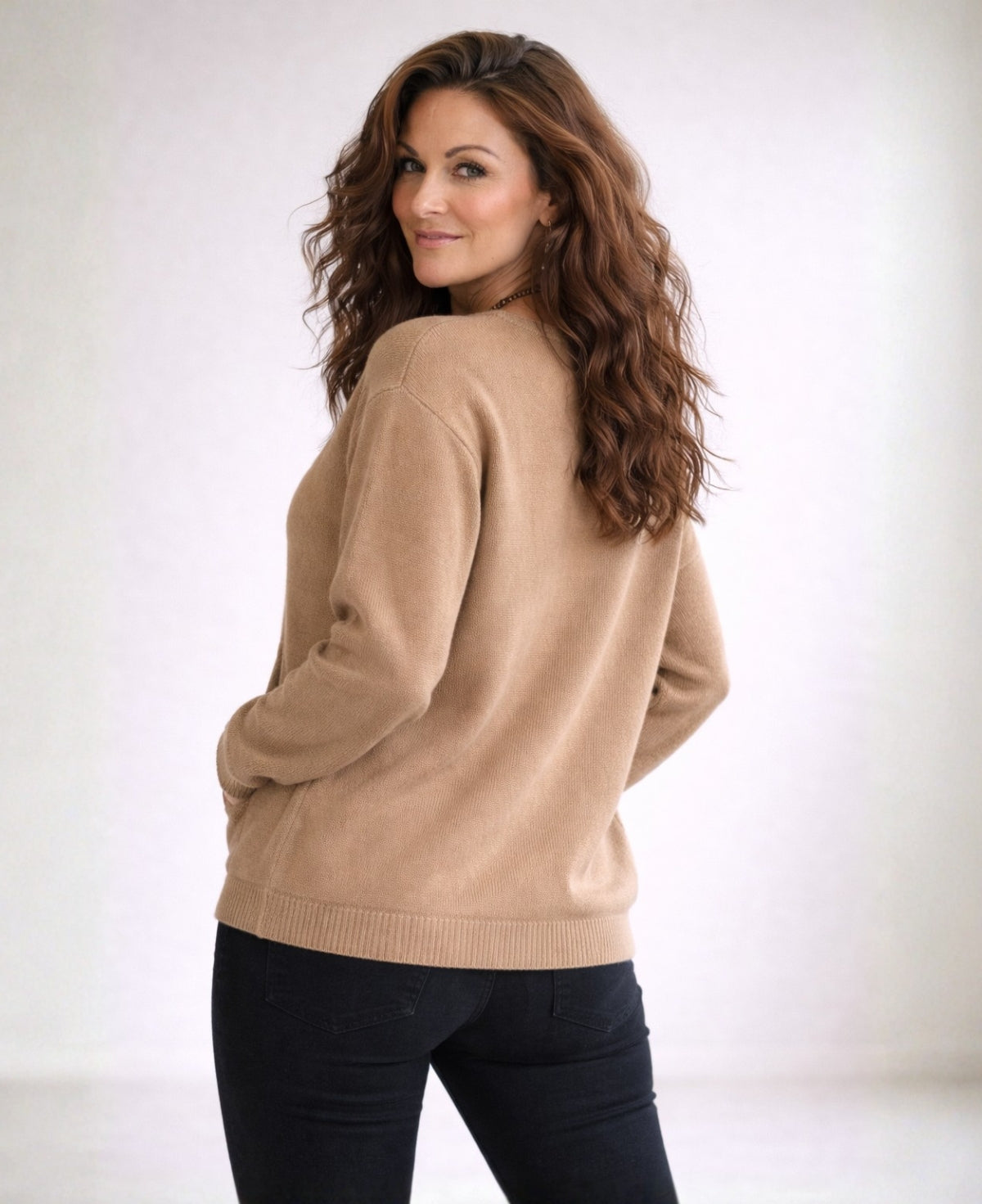 Angled back view of camel cashmere V-neck sweater in minimalist studio
