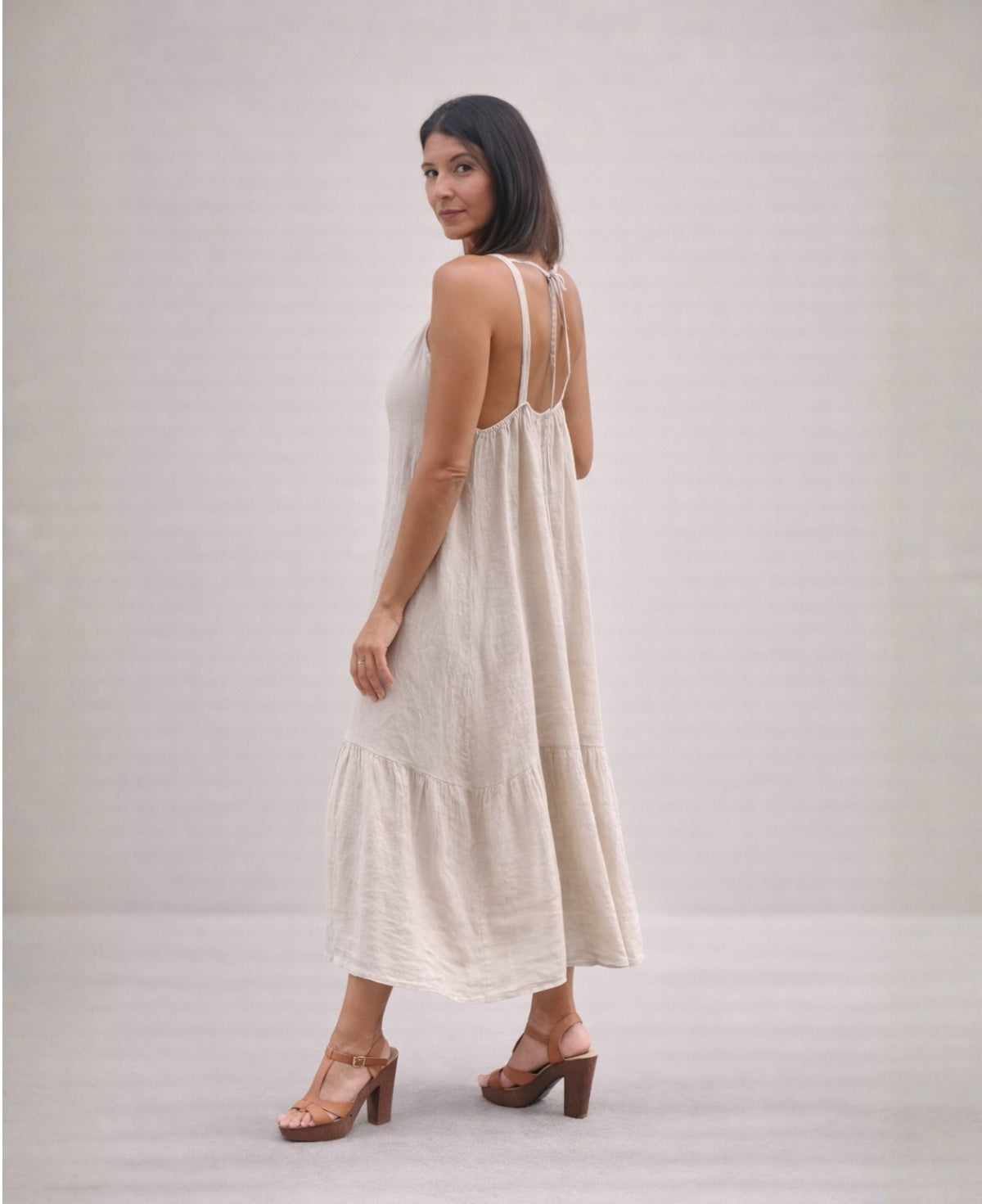 Side back view of the Cassey linen dress in beige, showing flowing linen fabric, tiered skirt and open back detail.