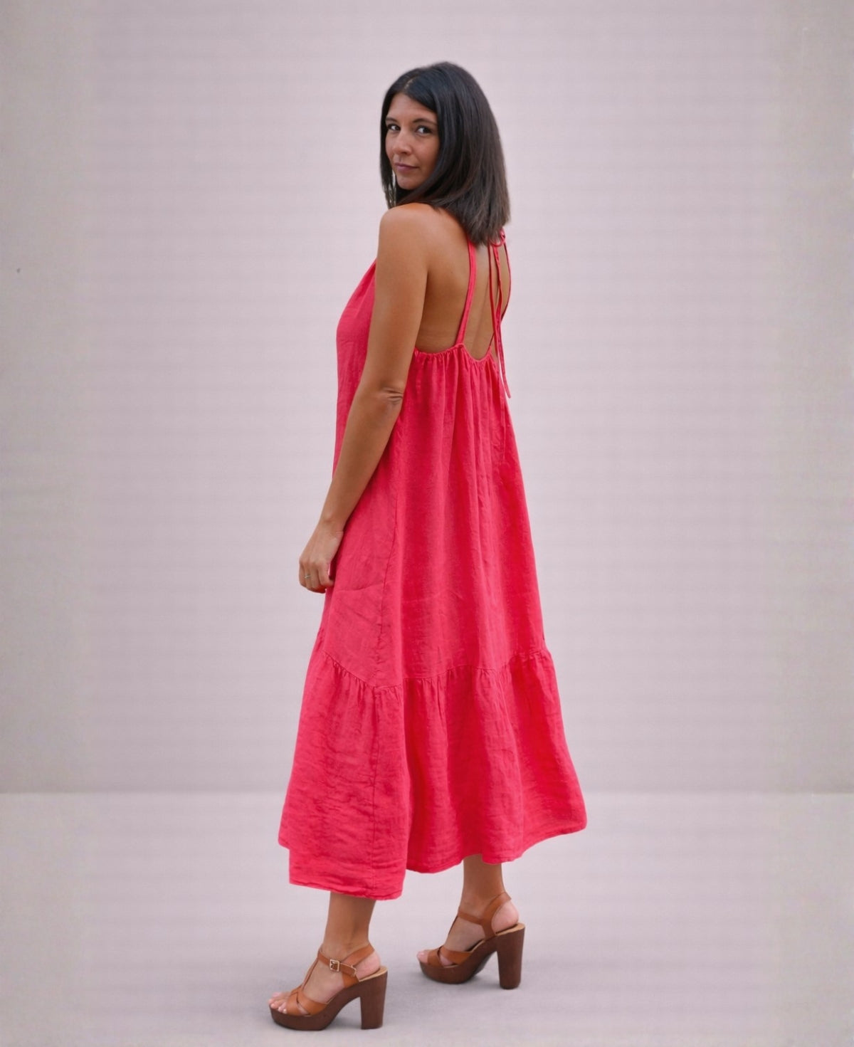 Back angled view of the Cassey linen dress in strawberry pink, showing adjustable straps, tie-back feature and soft linen movement.