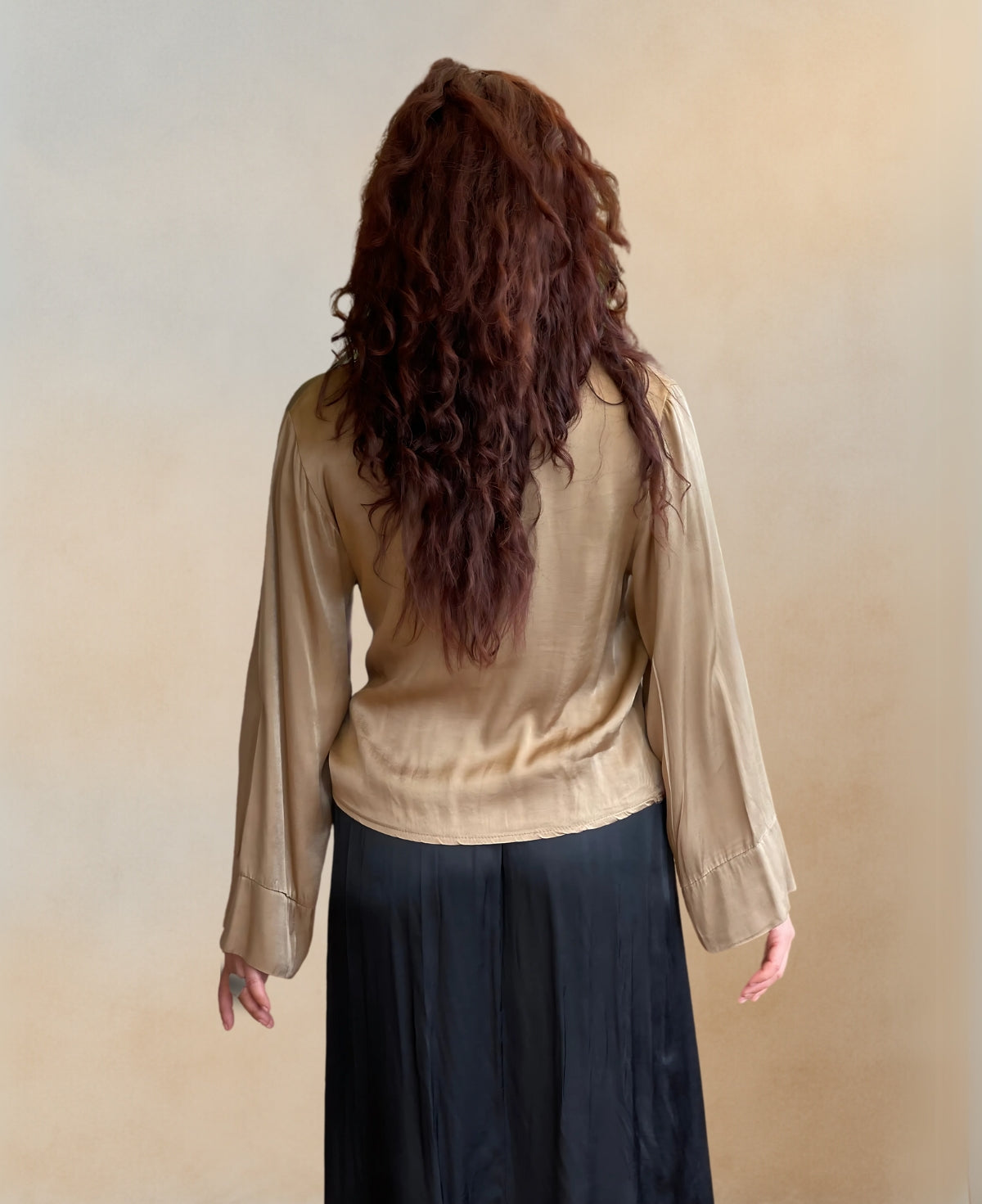 Back view of the stunning satin crossover blouse in gold with a crossover V-neck, shirt collar, and side bow tie waist belt. Long sleeves with wide cuffs create a chic, relaxed silhouette