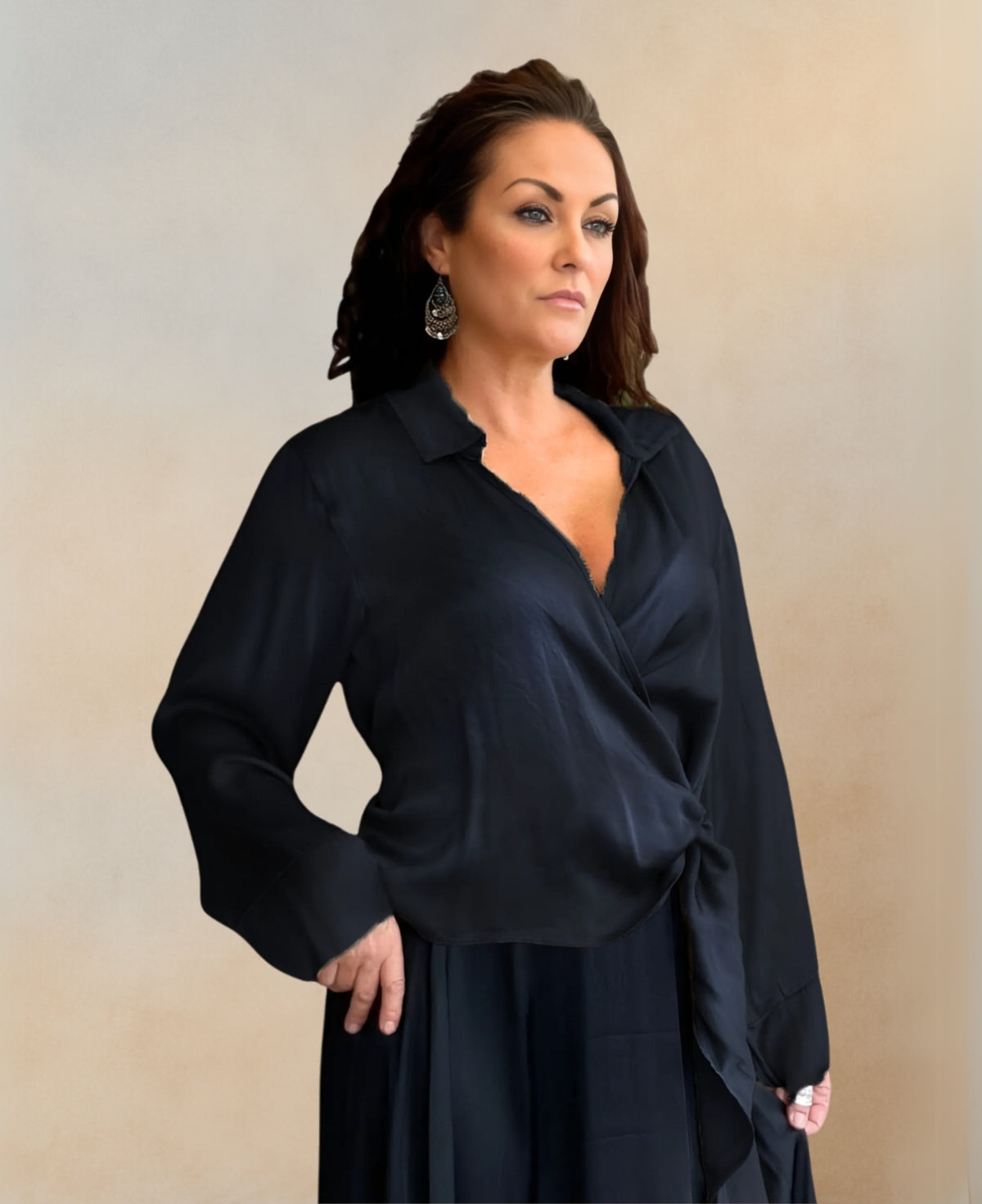 Luxurious satin crossover blouse in black, featuring a shirt collar, crossover V-neck design, and side bow tie waist belt. Long sleeves with wide cuffs complete this elegant, relaxed fit.