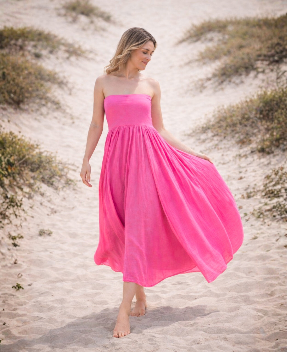 Cotton voile convertible maxi skirt worn as a strapless dress in fuchsia with voluminous flow on a beach setting