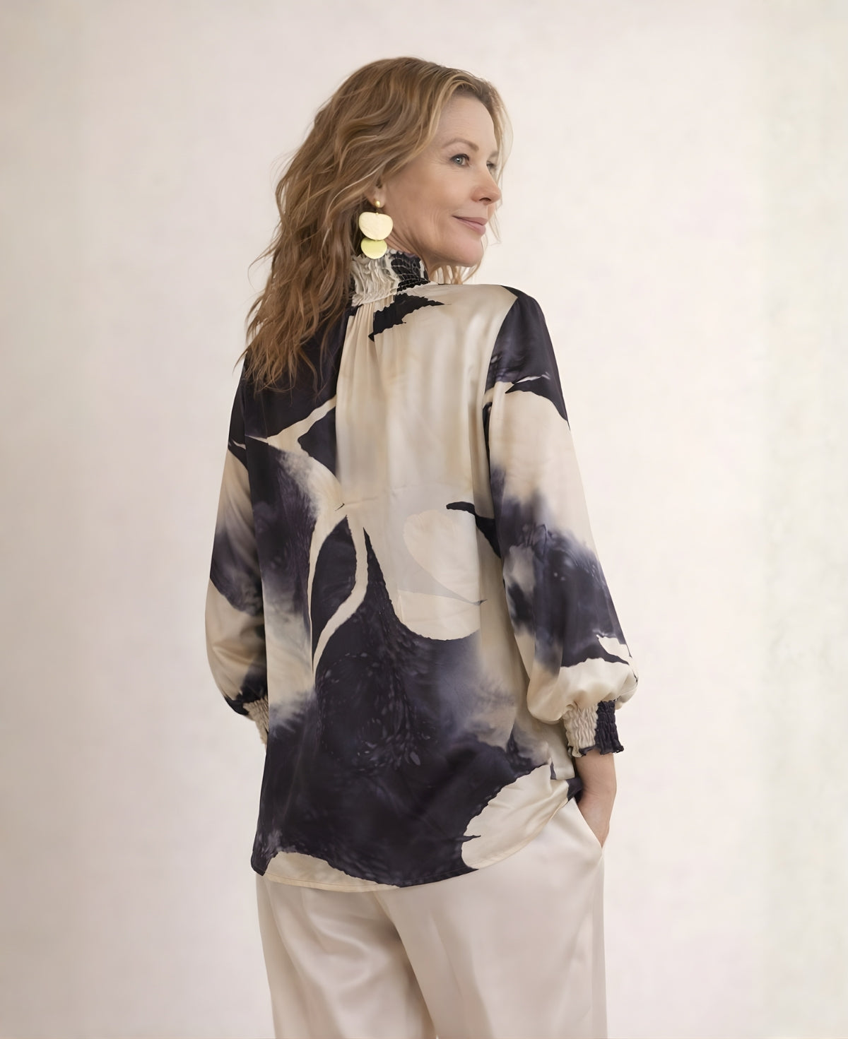 Back angled view of Cygnet satin blouse in black abstract print, showing loose drape over hips, gathered neckline and shirred cuffs.
