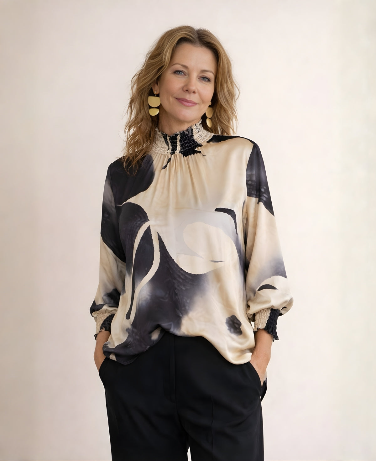 Relaxed front view of Cygnet satin blouse in black and cream abstract print, worn loose with black tailored pants and visible shirred neckline detail.