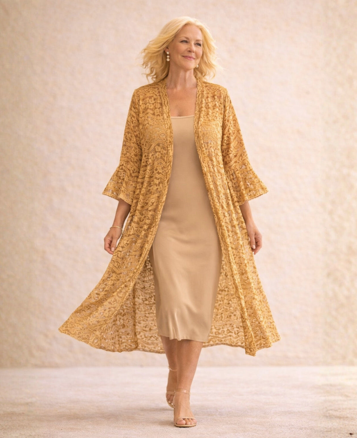 Blonde model walking in the Daniella Lace Kimono in Caramel, highlighting the flowing lace fabric and relaxed mid-calf silhouette on a soft limestone backdrop.