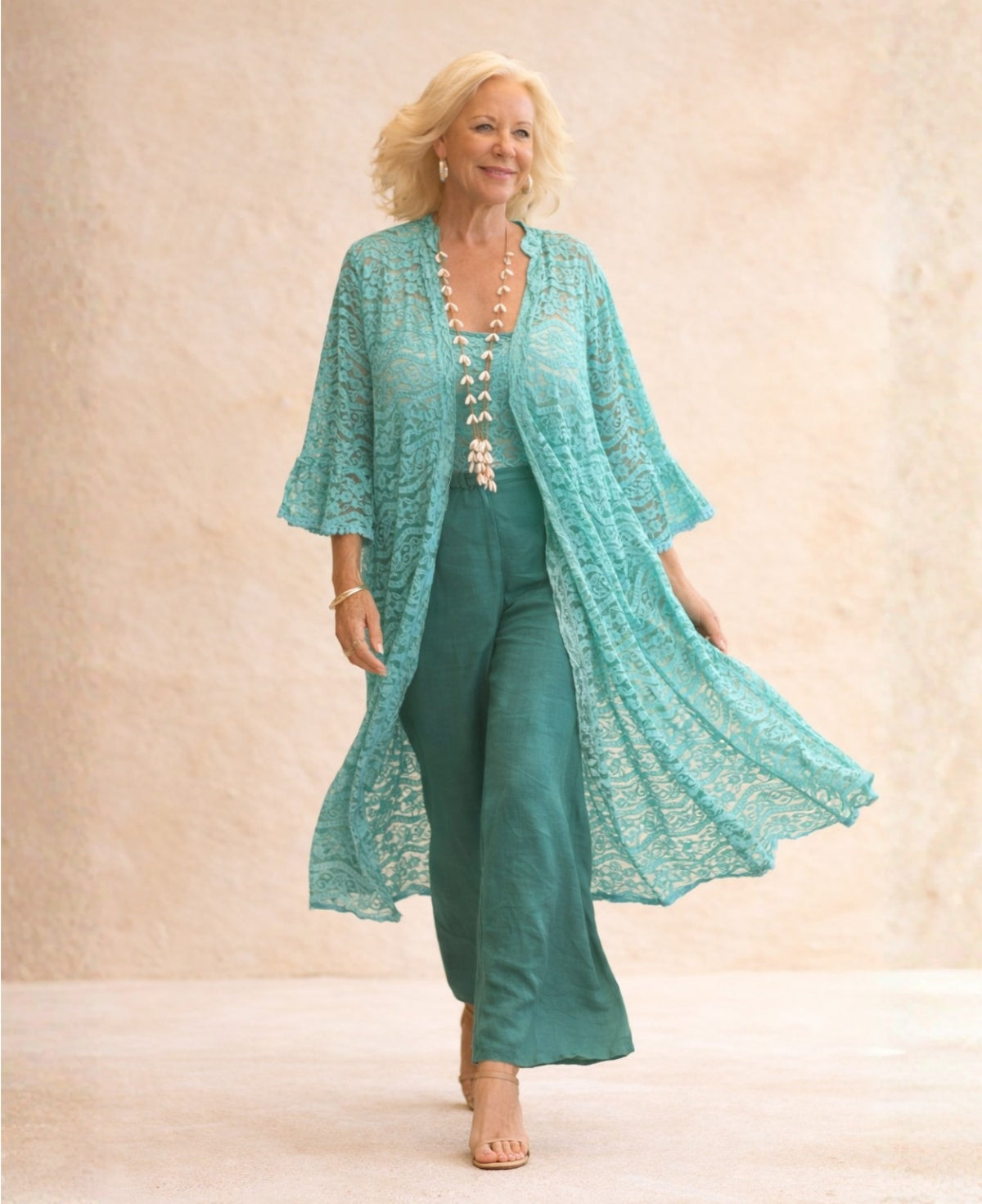 Blonde model walking forward in the Tiffany Daniella Lace Kimono, showing the flowing cotton lace fabric and sheer movement against a soft sandstone backdrop.