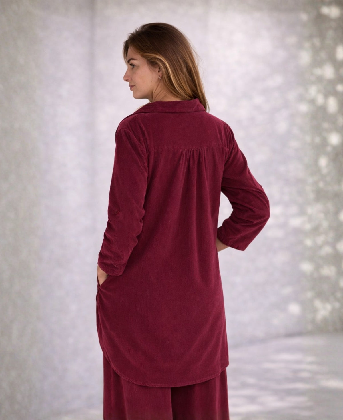 Back view of the Dawn corduroy shirt in black, worn with matching pants, showing the yoke seam, gentle gathers, long curved back hem, and fine corduroy ribbing.