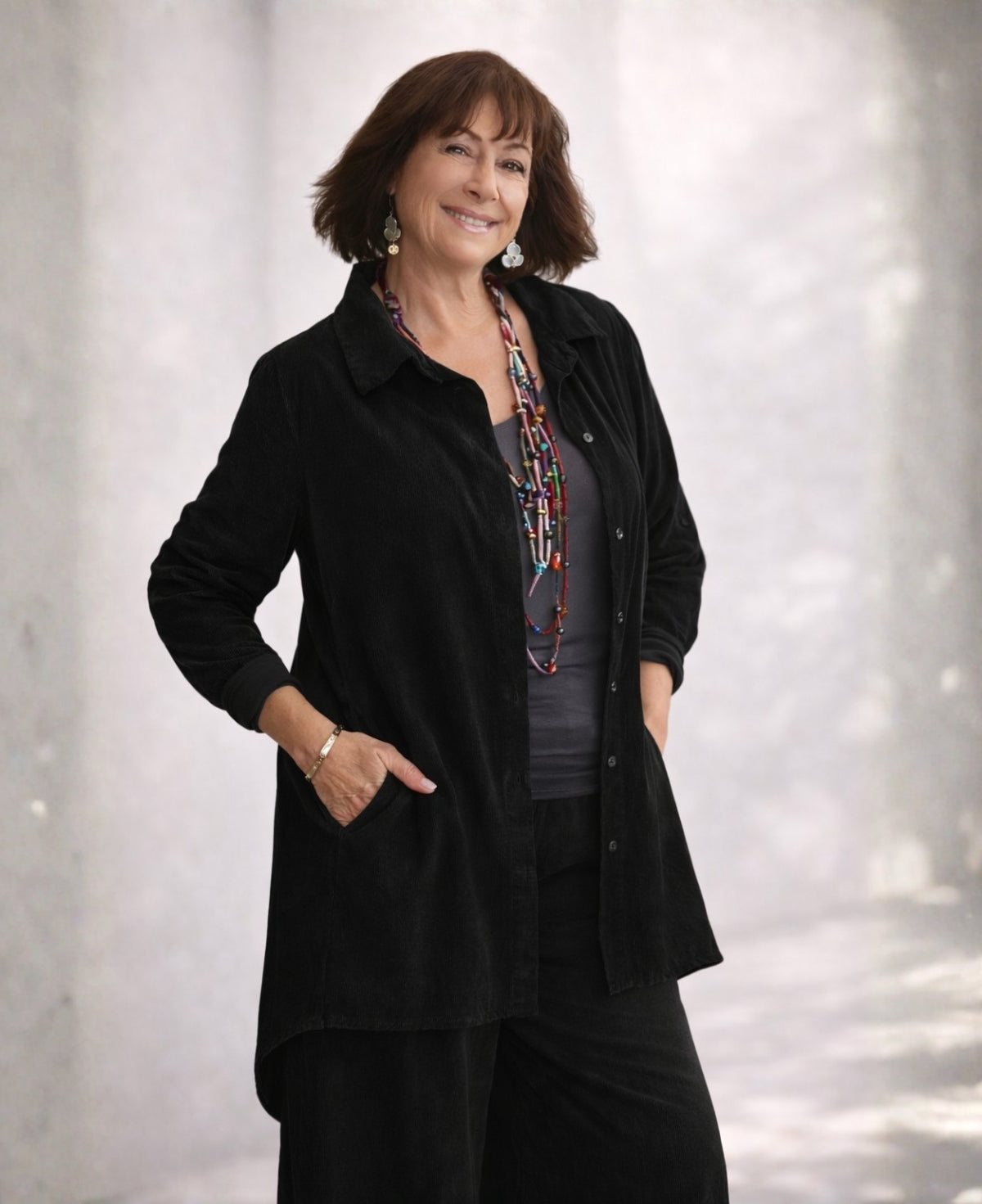 Front view of the Dawn corduroy shirt in desert sage styled on a mature woman, showing fine corduroy ribbing, side seam pockets, roll-tab sleeves, and an easy relaxed silhouette.