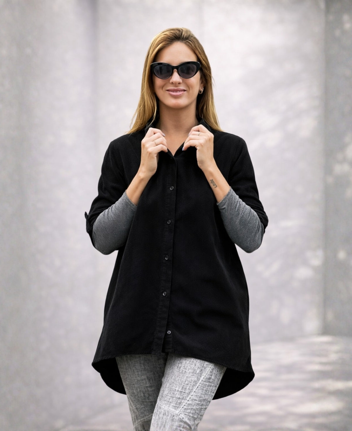 Model wearing the black Dawn Corduroy Shirt with fine ribbed texture, styled over a grey top and light grey pants, photographed against a soft neutral studio background.