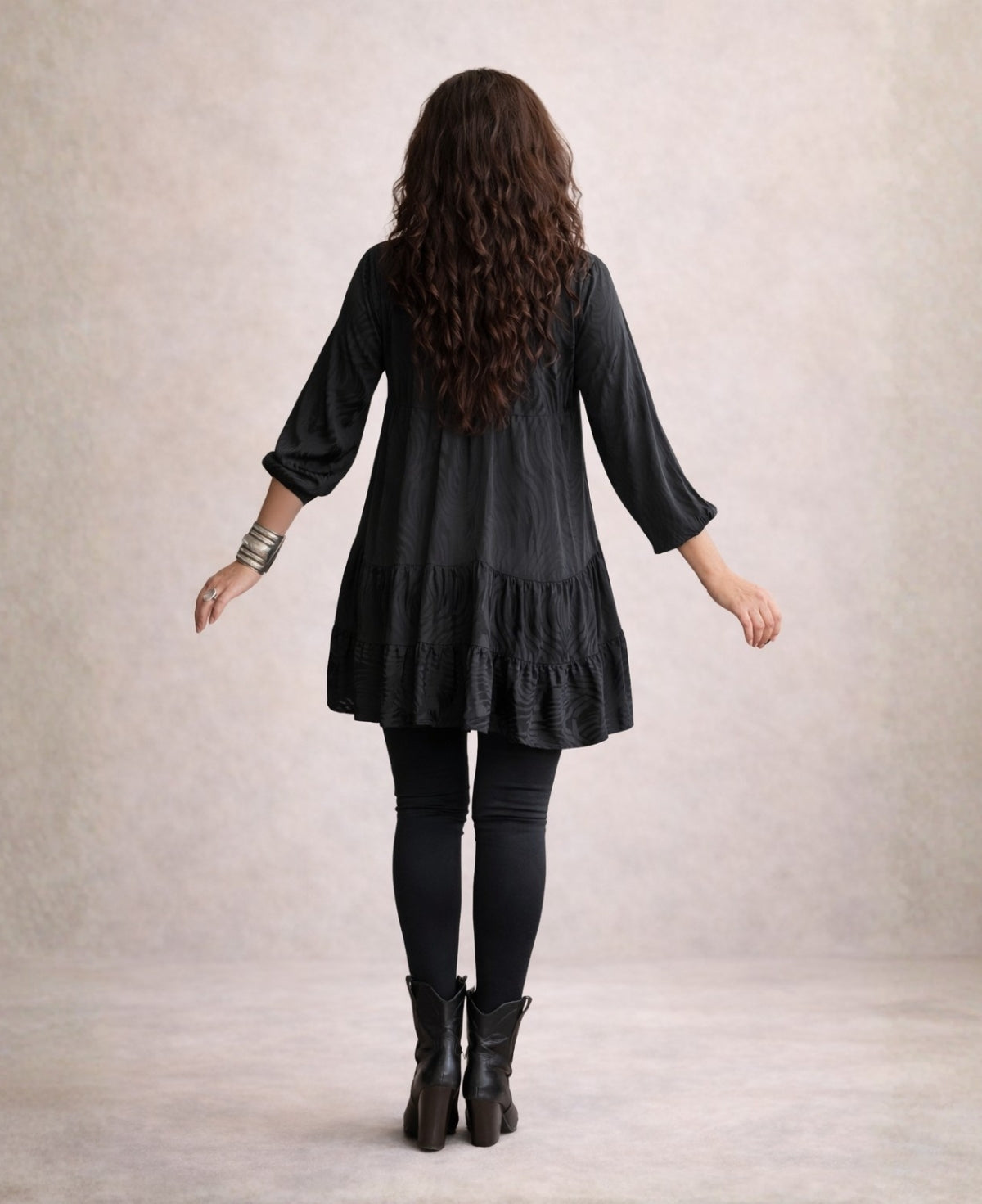 Back view of the black Eden Pattern satin top mini dress highlighting the flowing tiered design and embossed satin fabric.