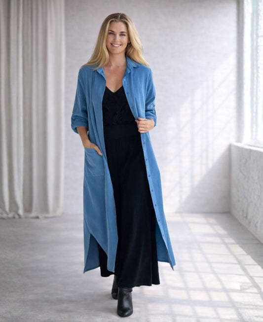 Model wearing the Empire Fray fine-rib corduroy shirt dress in Blue Haven layered over a black dress in a soft studio background.