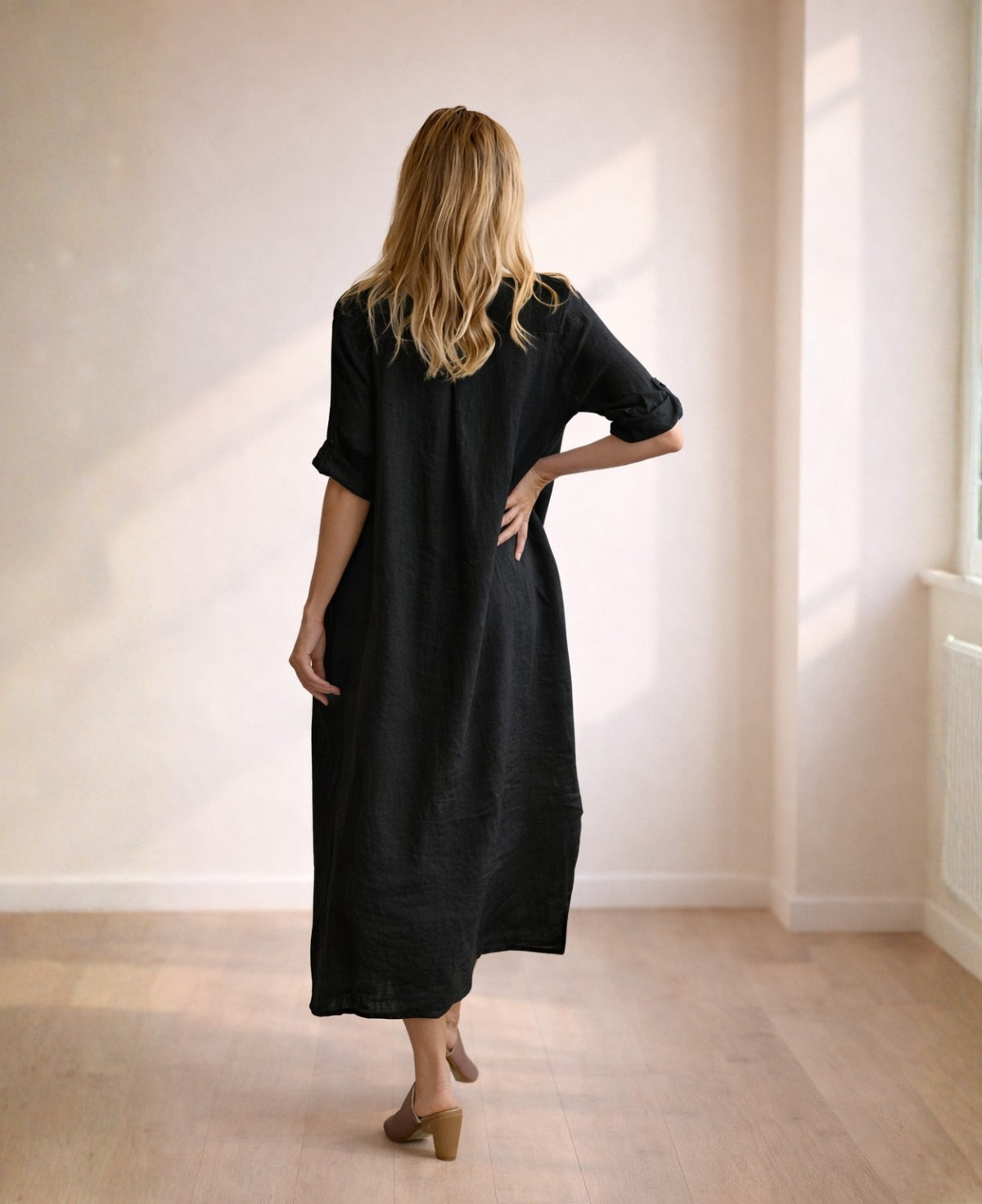 Back view of black linen Empire Jac-Dress with soft drape, rolled sleeves and breathable linen texture in minimalist studio setting.