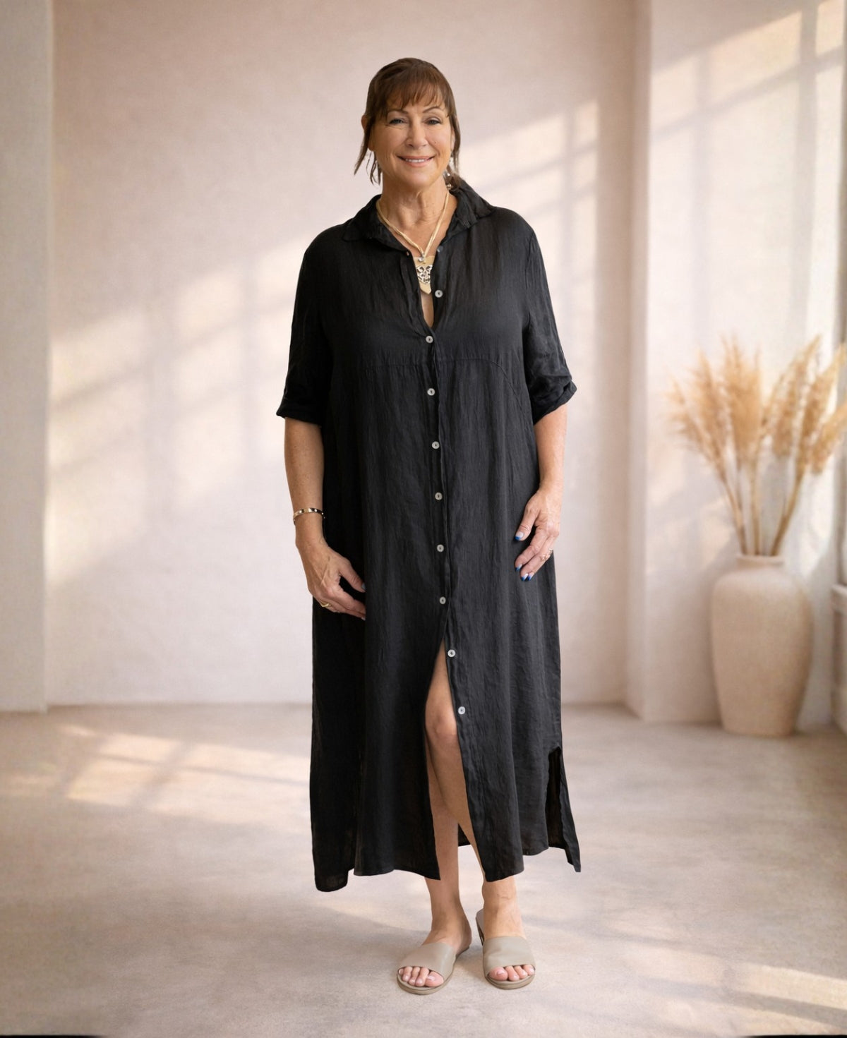 Front view of black linen Empire Jac-Dress with button front, empire waist seam and side split, styled in warm neutral studio.