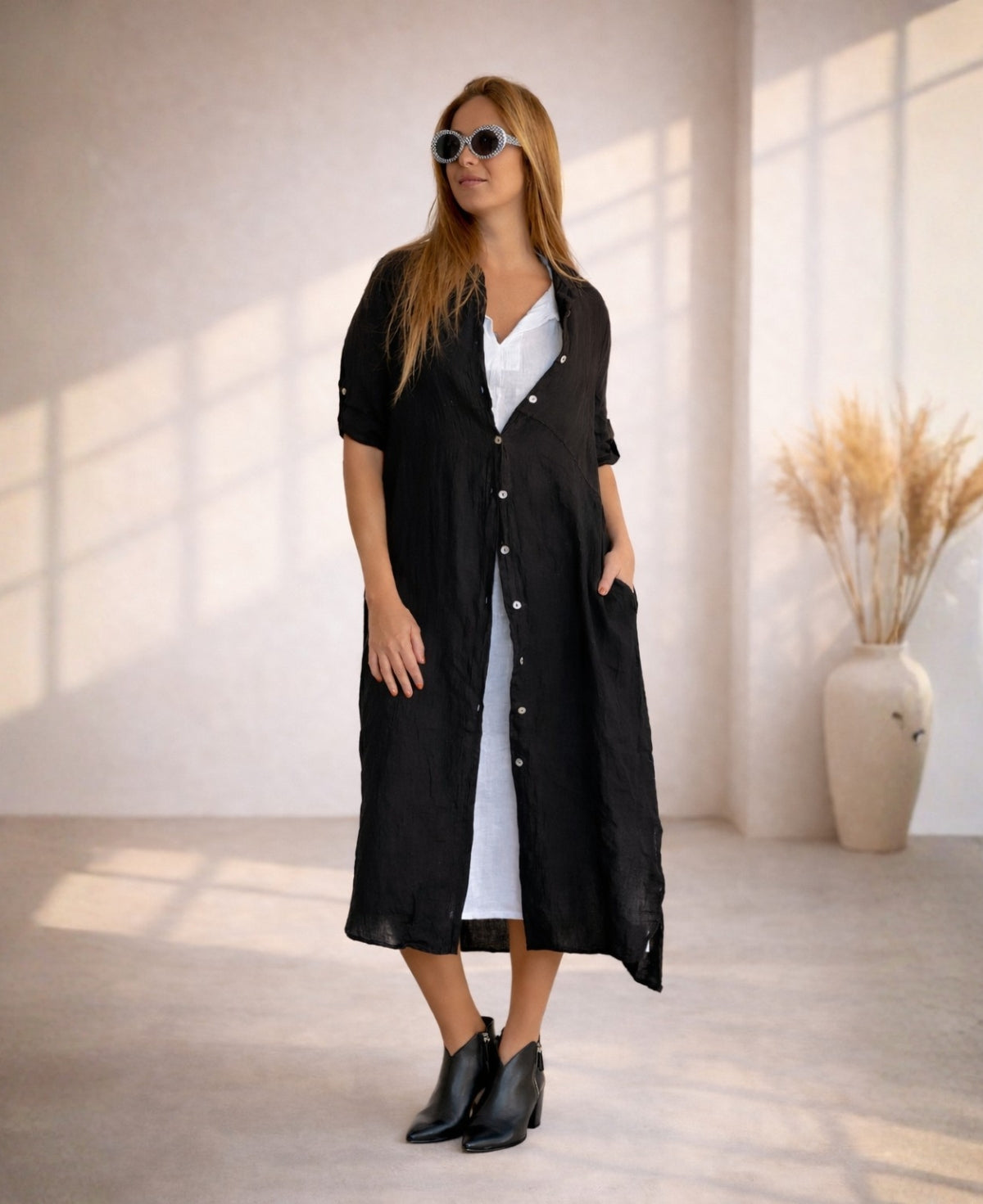 Black linen Empire Jac-Dress worn open over white linen dress, showing empire seam, button detail and relaxed drape in warm studio light.