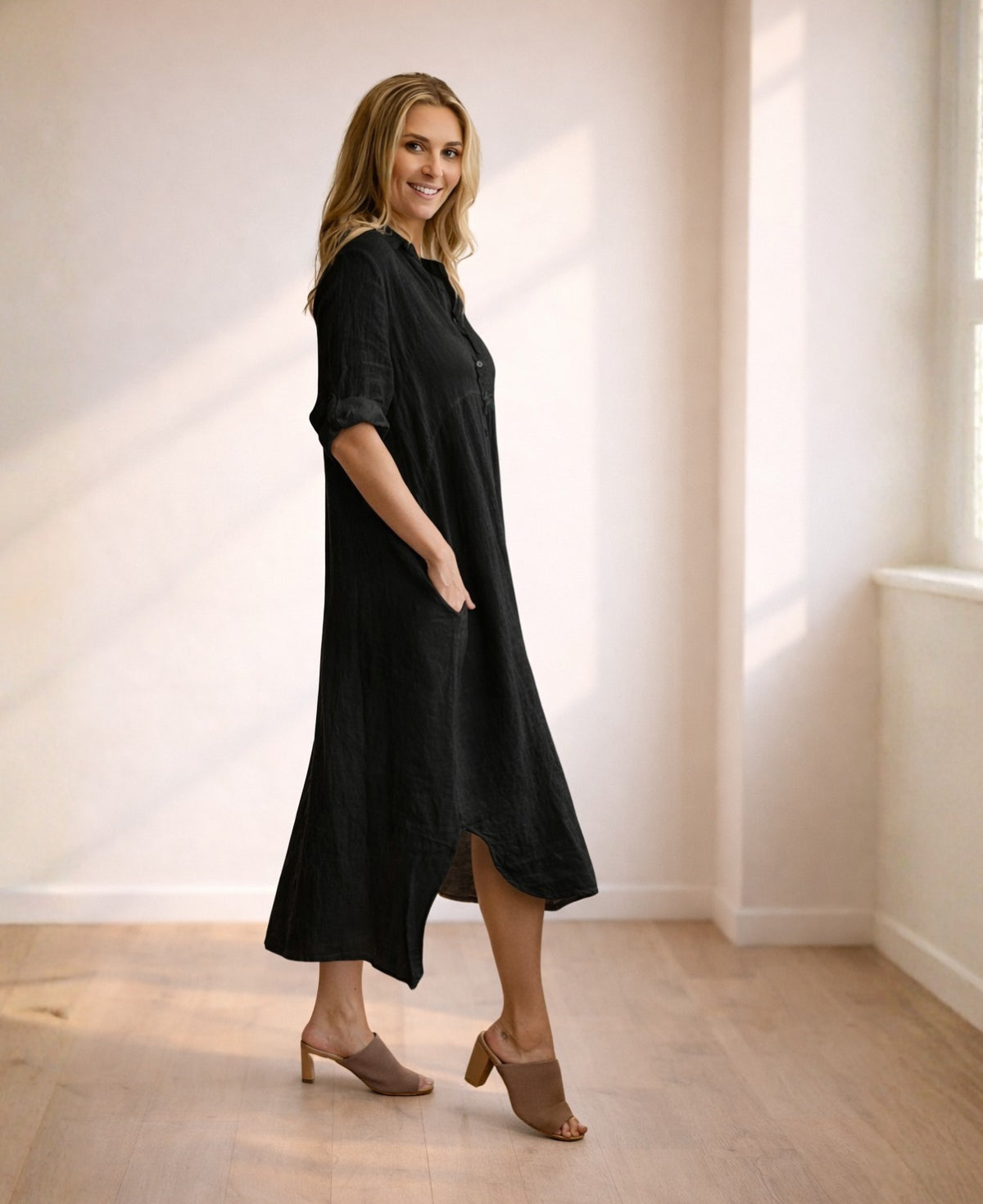 Side view of black linen Empire Jac-Dress showing relaxed A-line shape, empire seam and natural linen texture in warm studio light.