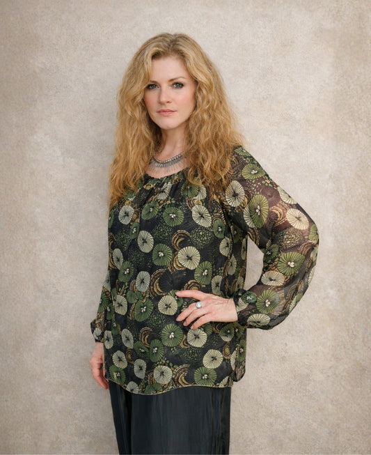 Woman wearing the Fern Silk Blouse with botanical green print, sheer silk sleeves and relaxed fit, styled with black wide leg pants