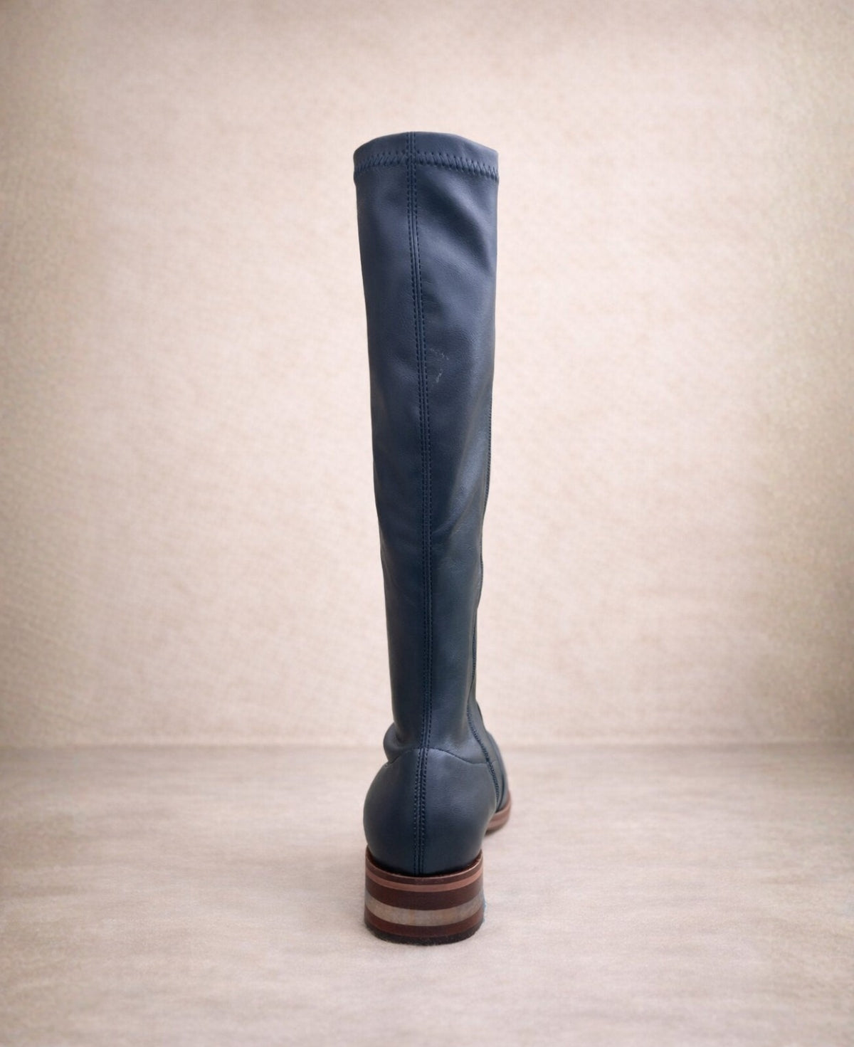 Back view of navy knee-high stretch boot showing clean stitching, fitted shaft, and layered heel detail.