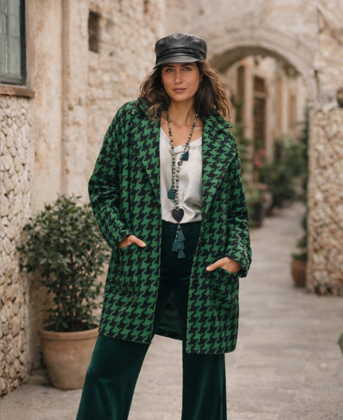 Model wearing a green houndstooth coat styled with velvet wide leg pants in a Mediterranean street setting, Italian inspired women’s winter fashion in Australia.