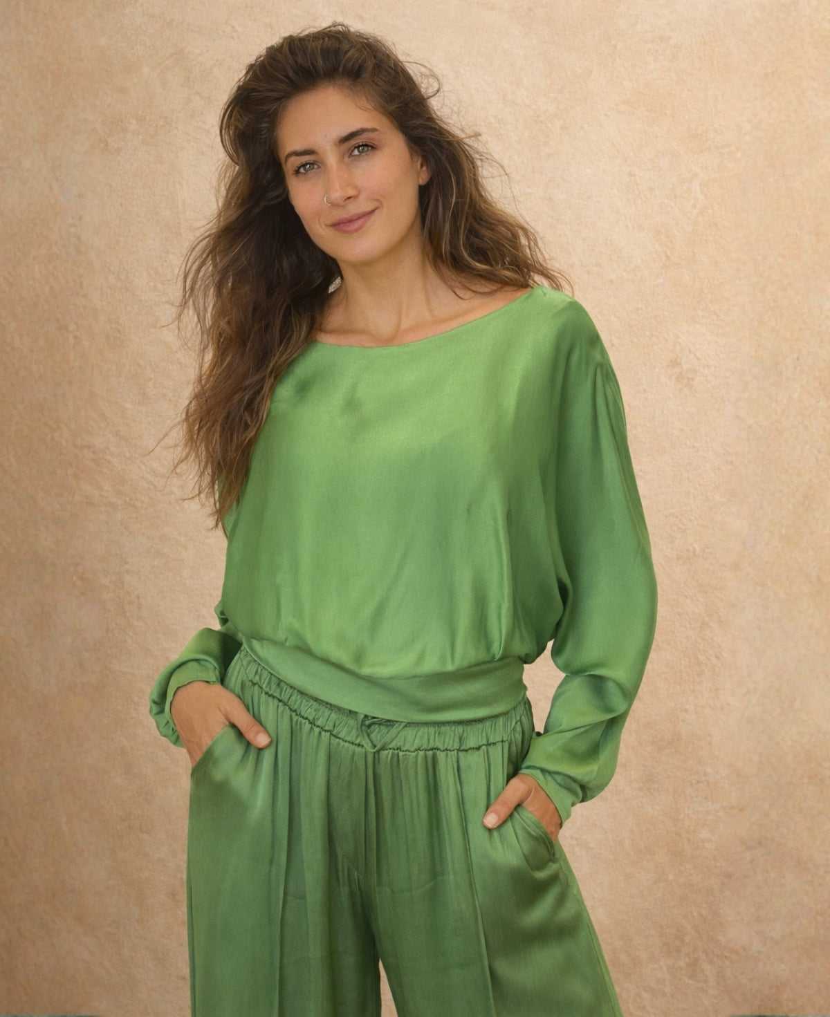 Close 3/4 view of green satin keyhole top showing soft draped neckline, long sleeves and elastic waist, styled with matching satin pants.