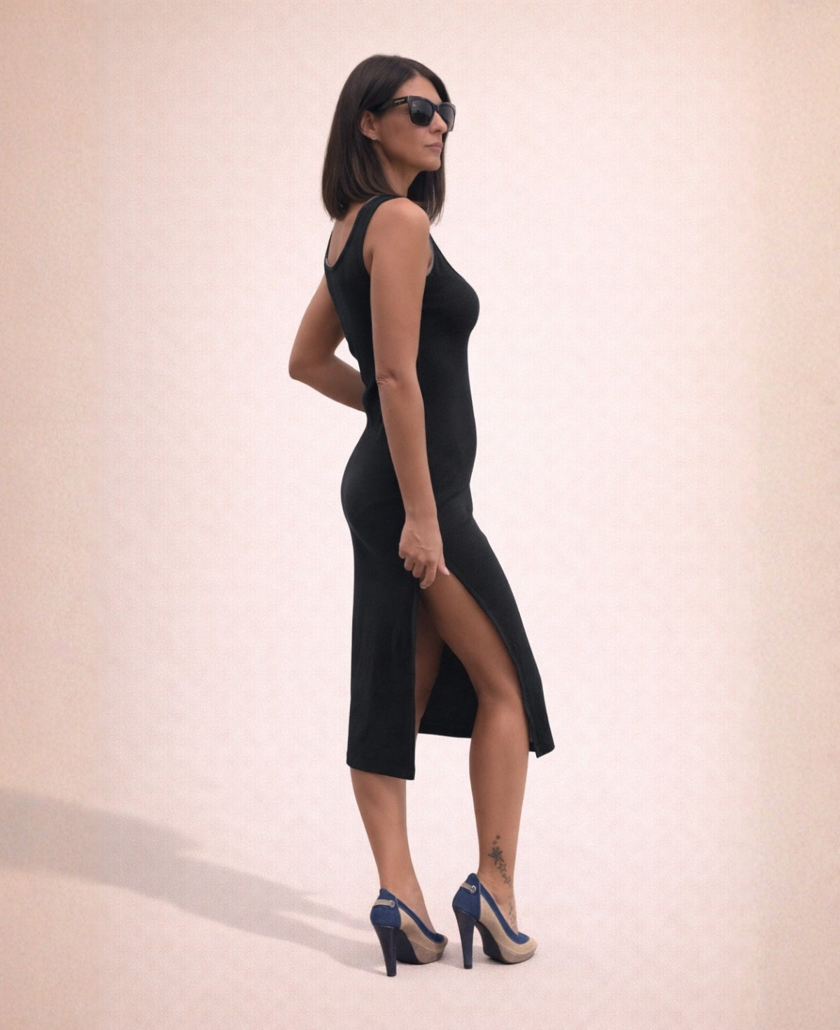 Woman wearing black ribbed cotton jersey Hollywood Dress with side slit, side view on minimalist studio background