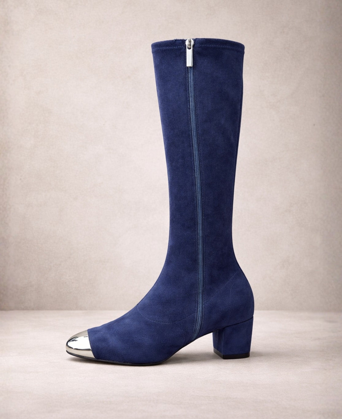 Side view of Hoppey navy suede knee high boots showing full-length side zip, block heel and silver toe cap on a soft architectural backdrop.