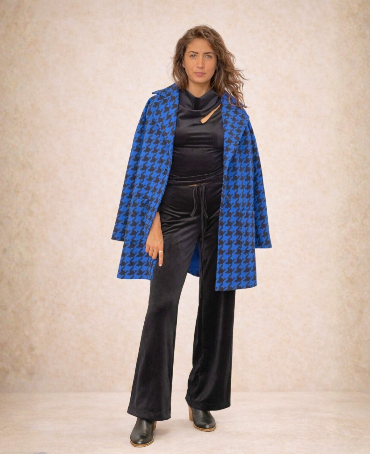 Woman wearing a blue houndstooth patterned coat over a black outfit on a beige background