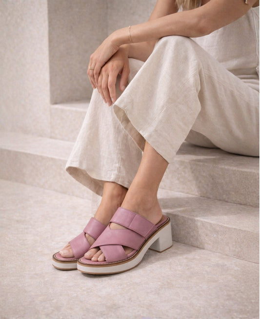 Woman wearing Jember Slide pink leather sandals with block heel, styled with stone cropped trousers in a modern architectural setting