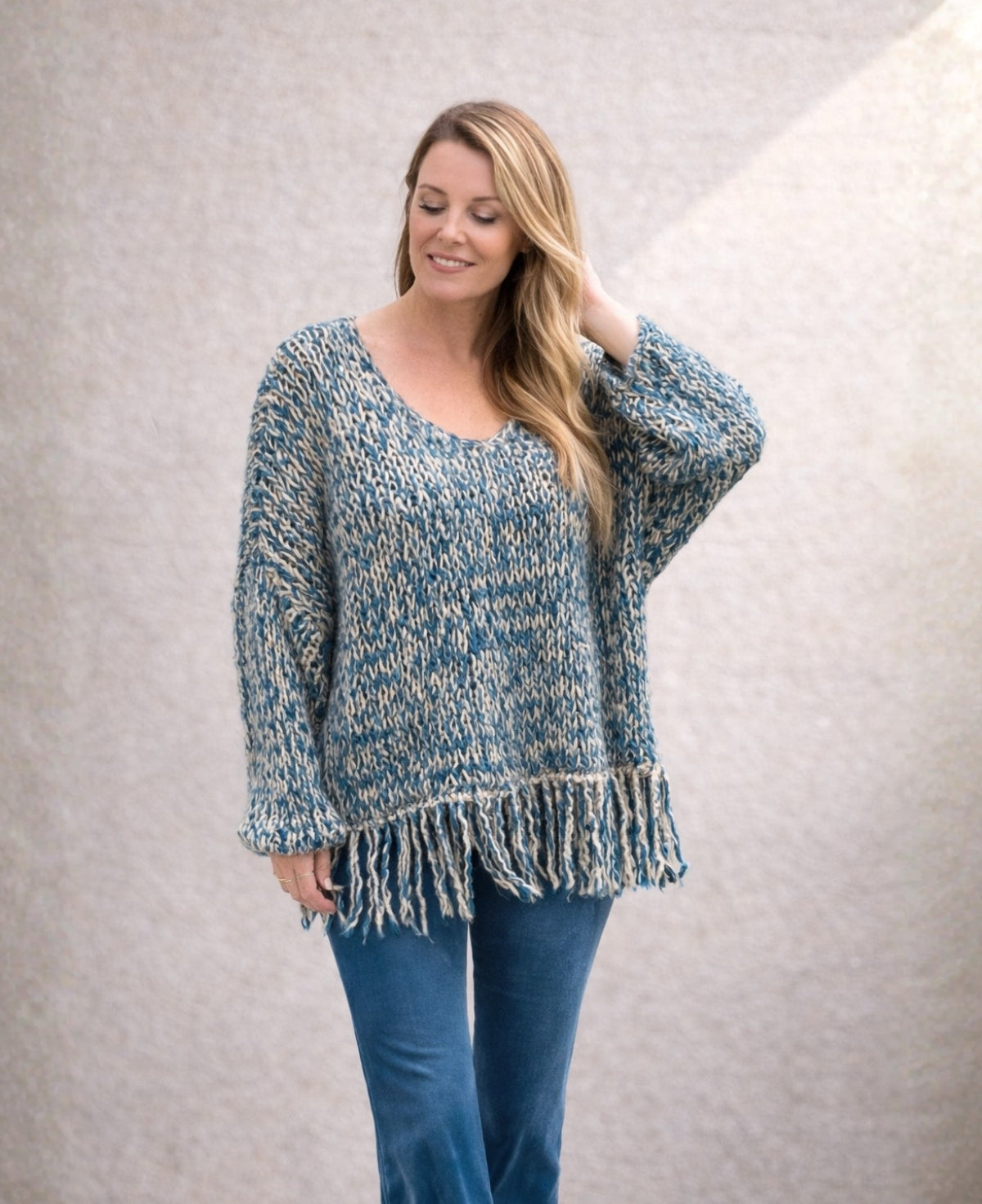 Relaxed half body view of blue mohair blend knit jumper with loose sleeves and fringe hem