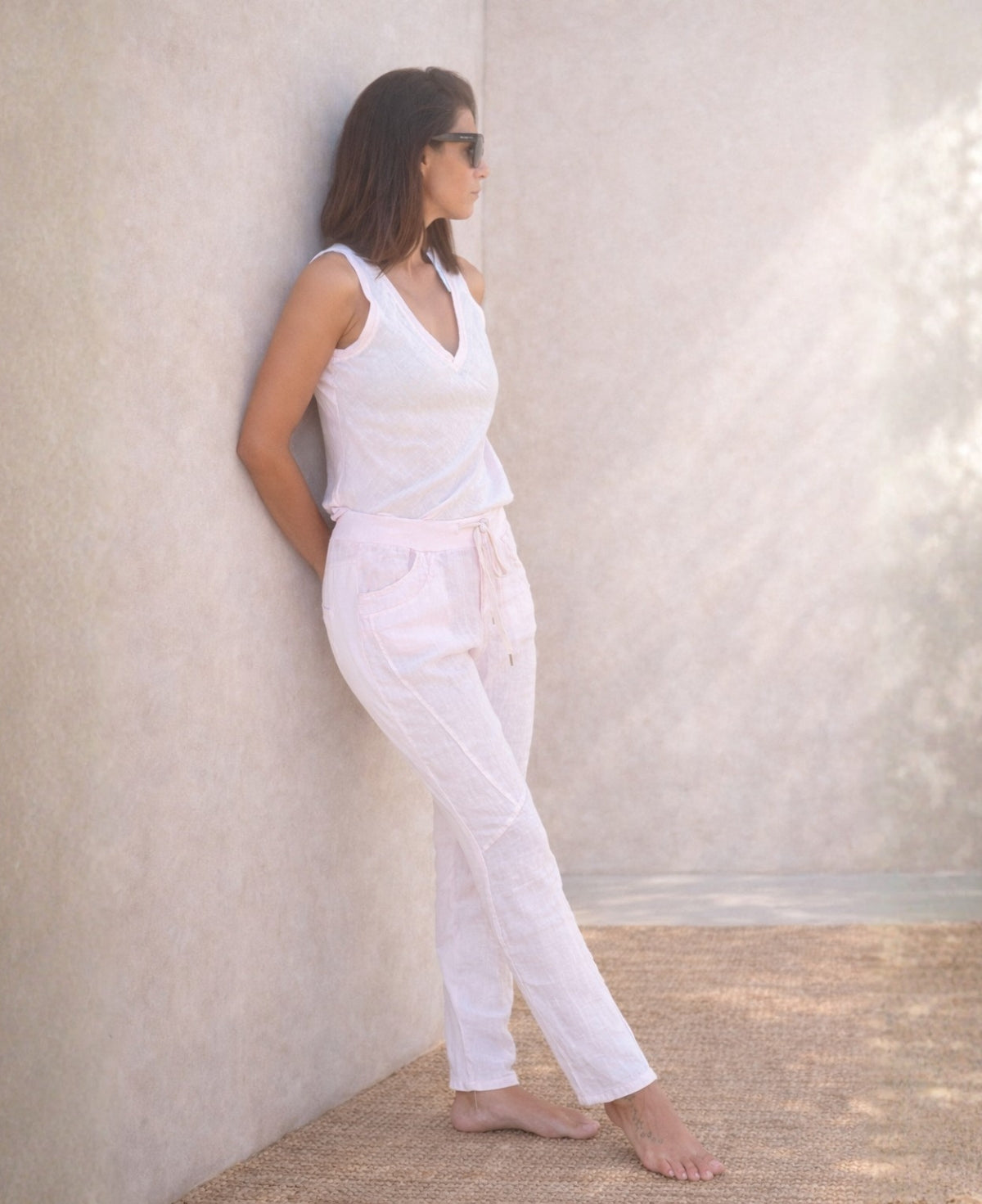 Full body side view of the Jordan Linen Pants in blush as model leans against wall, showing slim leg shape and stretch waist.