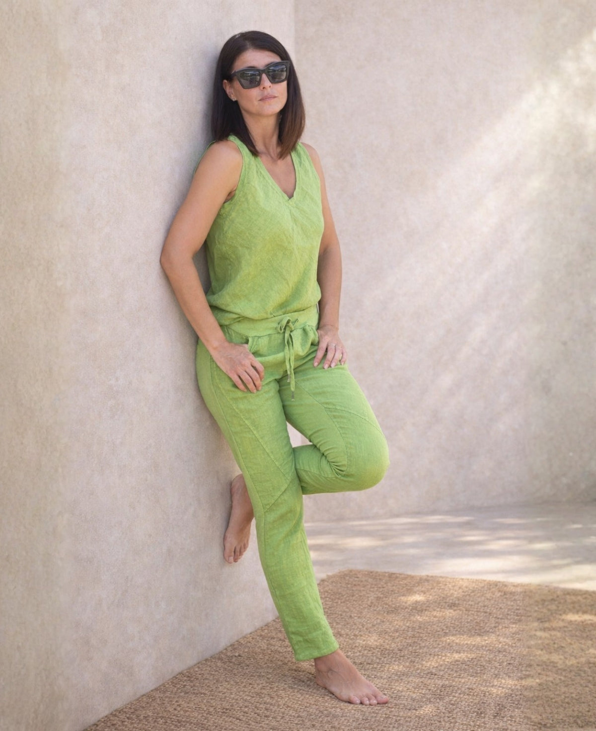 Full body angled front view of the Jordan Linen Pants in kiwi green leaning against wall, showing narrow leg fit and panel seams.