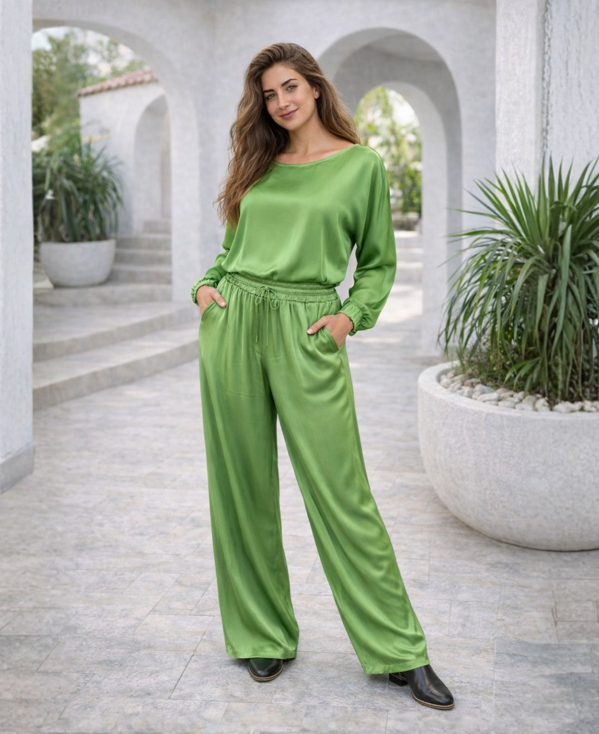 Apple green Juliette satin pants worn by model, featuring lightweight satin fabric and relaxed fit on a Mediterranean terrace